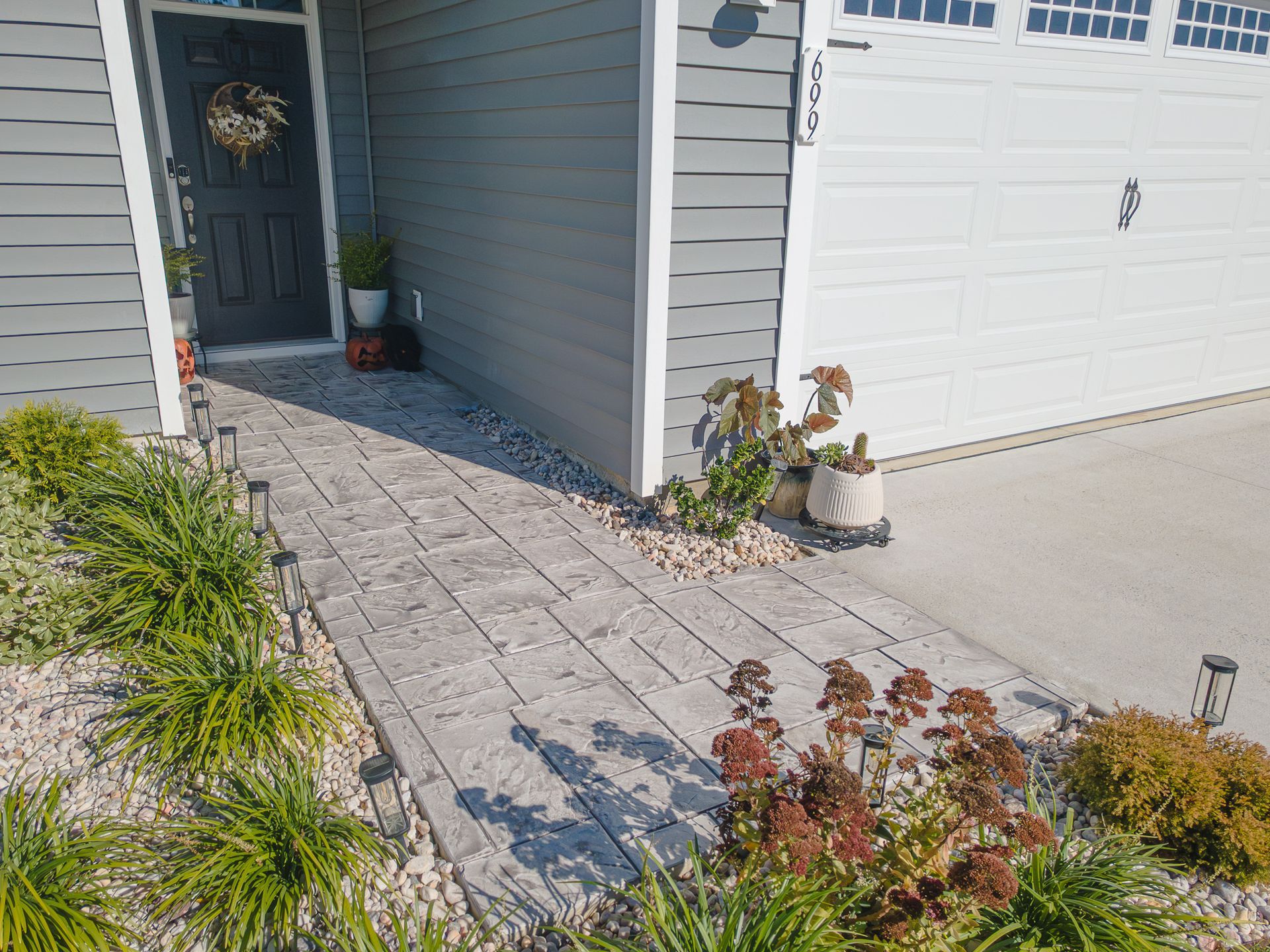 Front entry with gray paver walkway, white garage door, dark front door, and potted plants by the porch