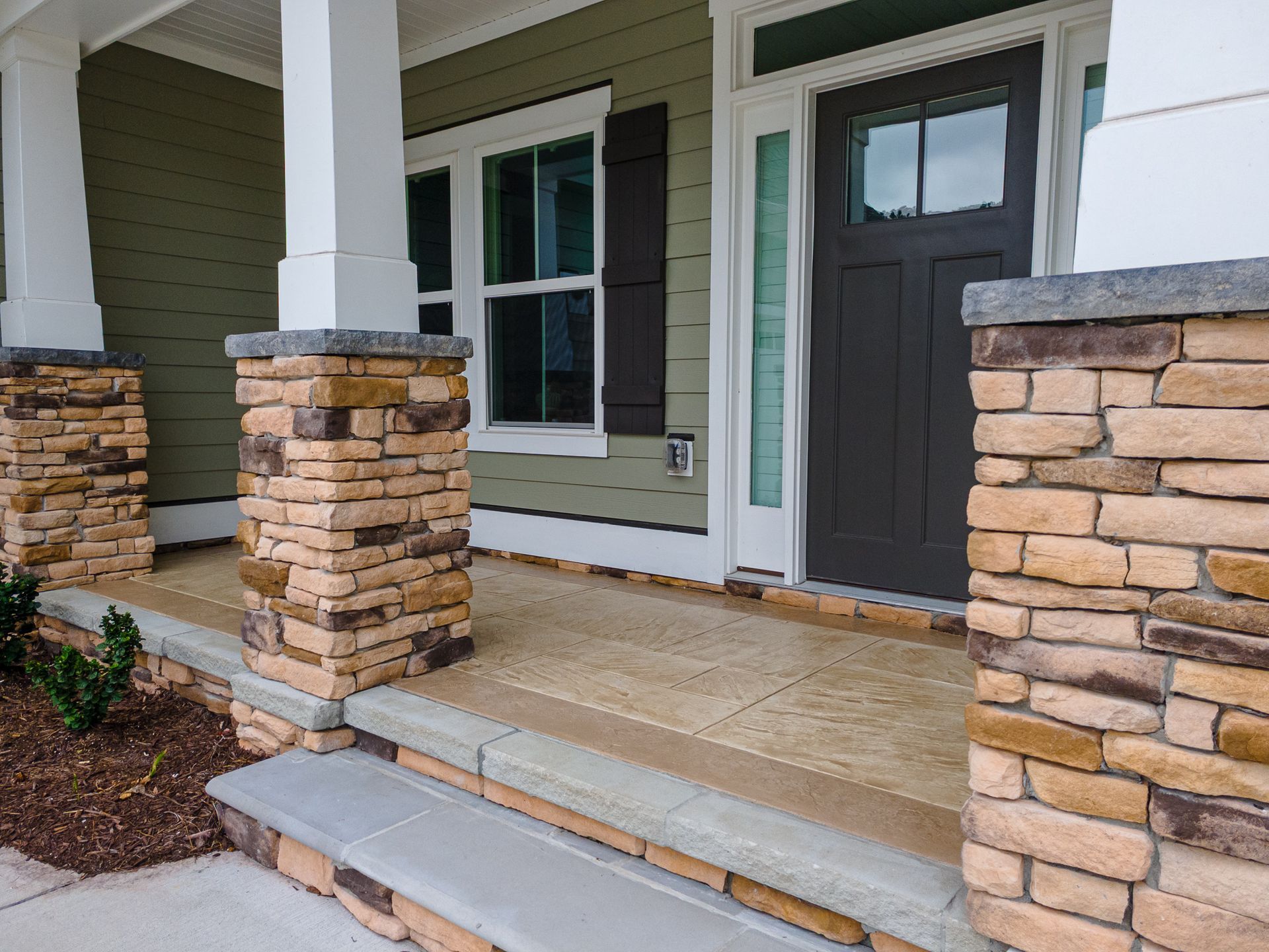 Front porch with stone columns, gray door, and steps leading to a house entrance.