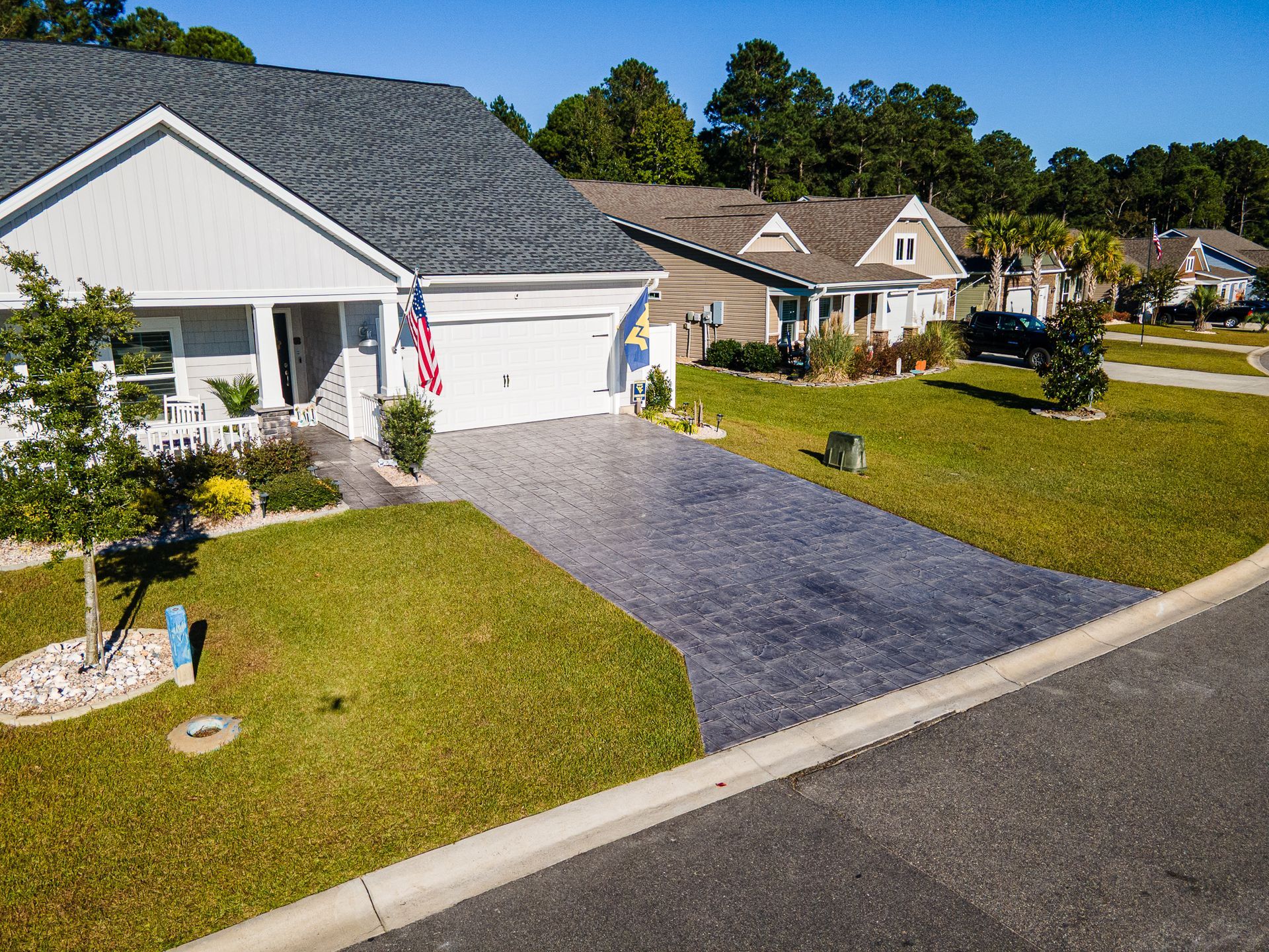 Suburban house with white garage, blue driveway, and an American flag on a sunny street