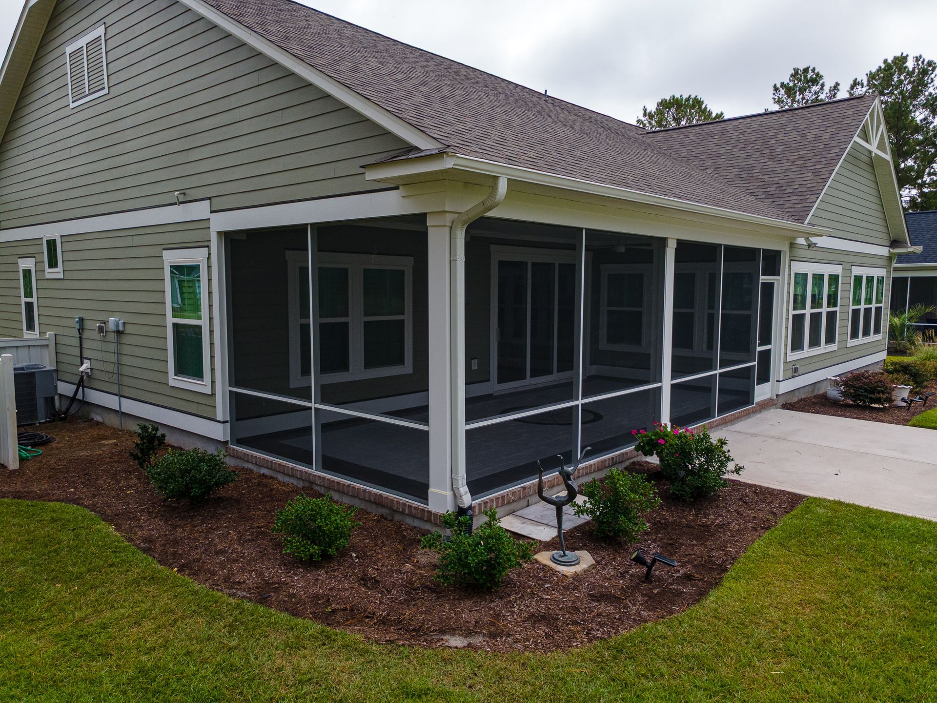 Single-story house with screened porch, green siding, and landscaped yard