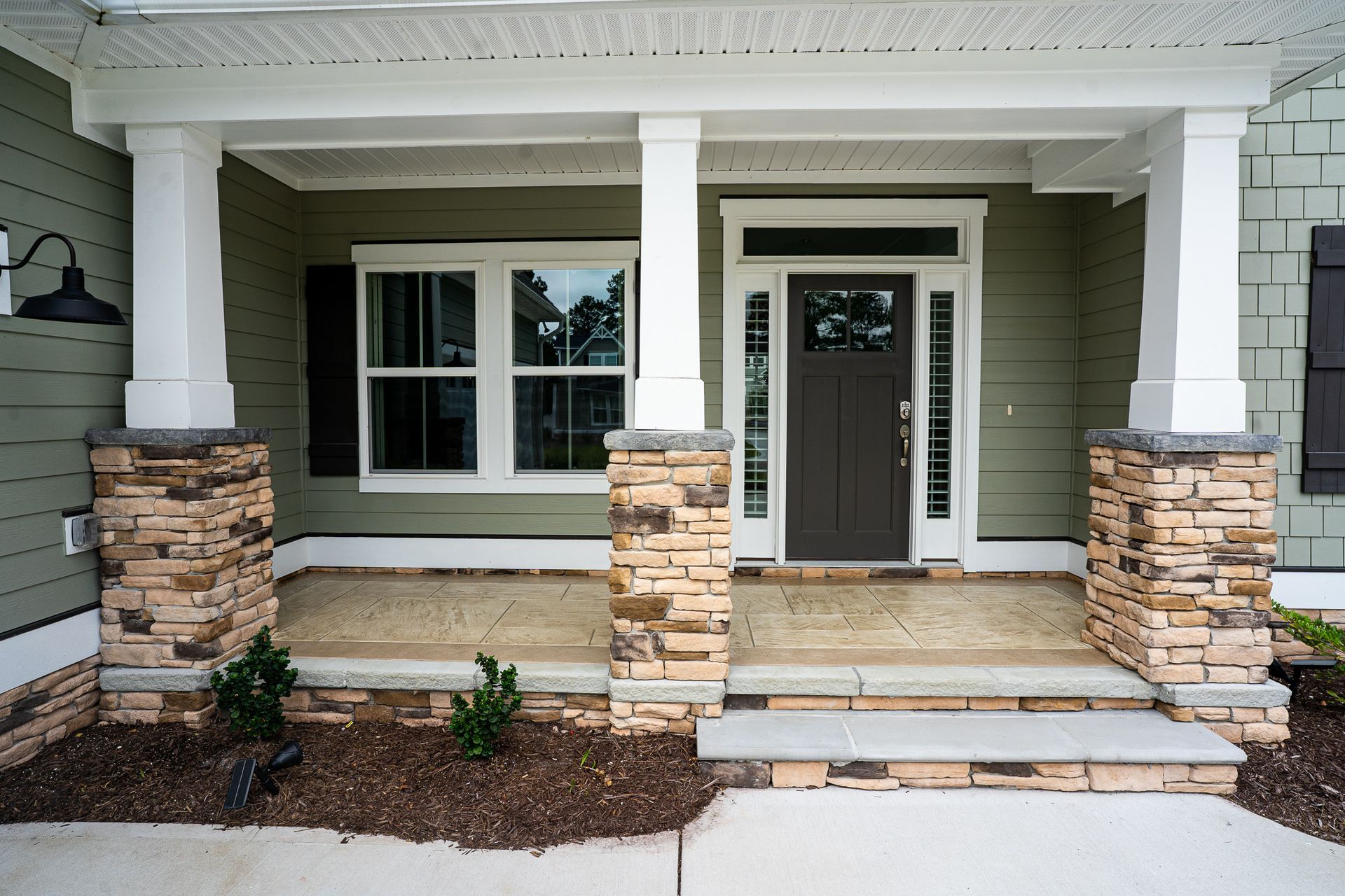 Front porch of a house with white columns, stone bases, steps, and a glass front door.