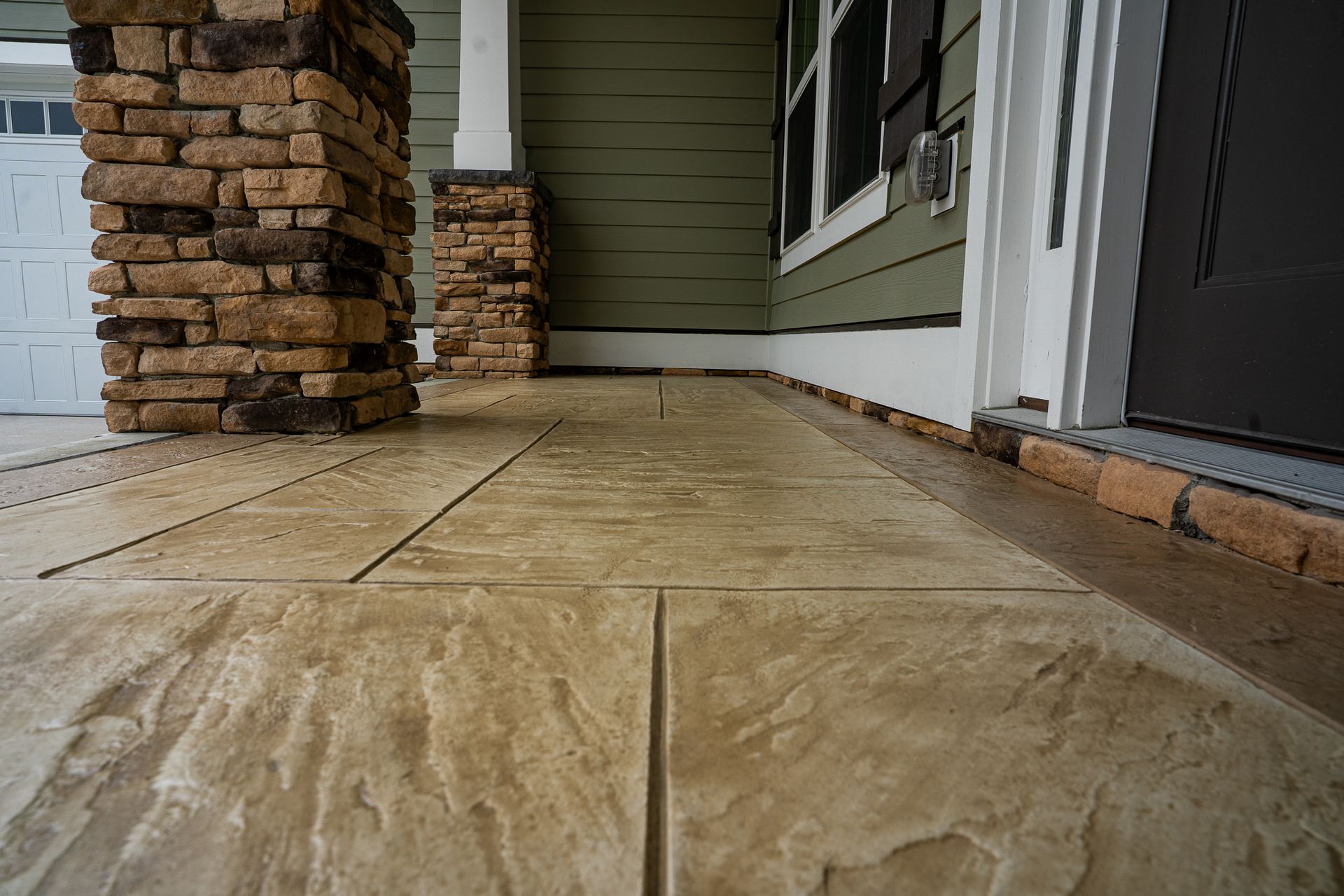 Front porch with tan stone tile, stacked stone columns, and white siding beside a screened door.