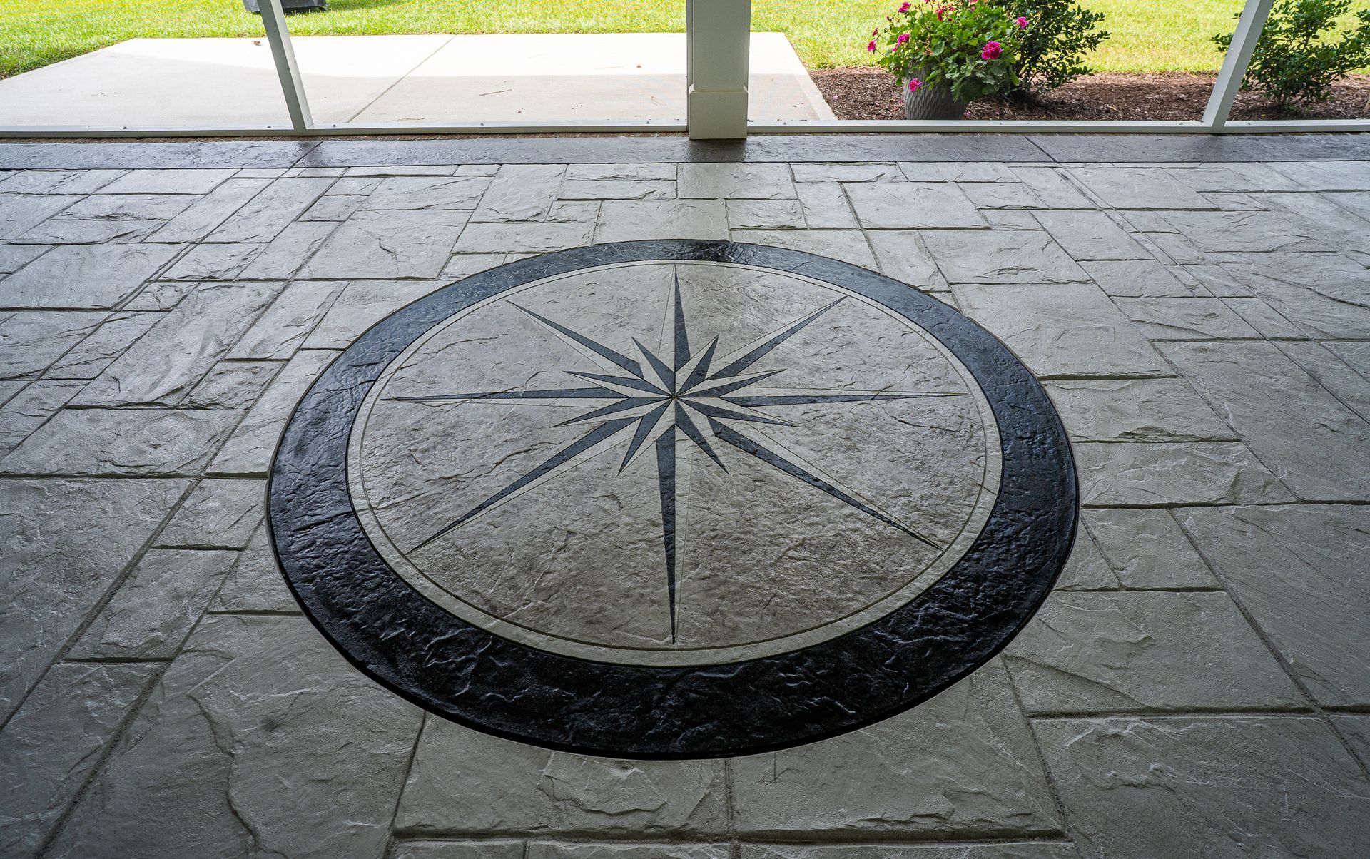 Stone compass rose set into a paved walkway under a covered outdoor area.