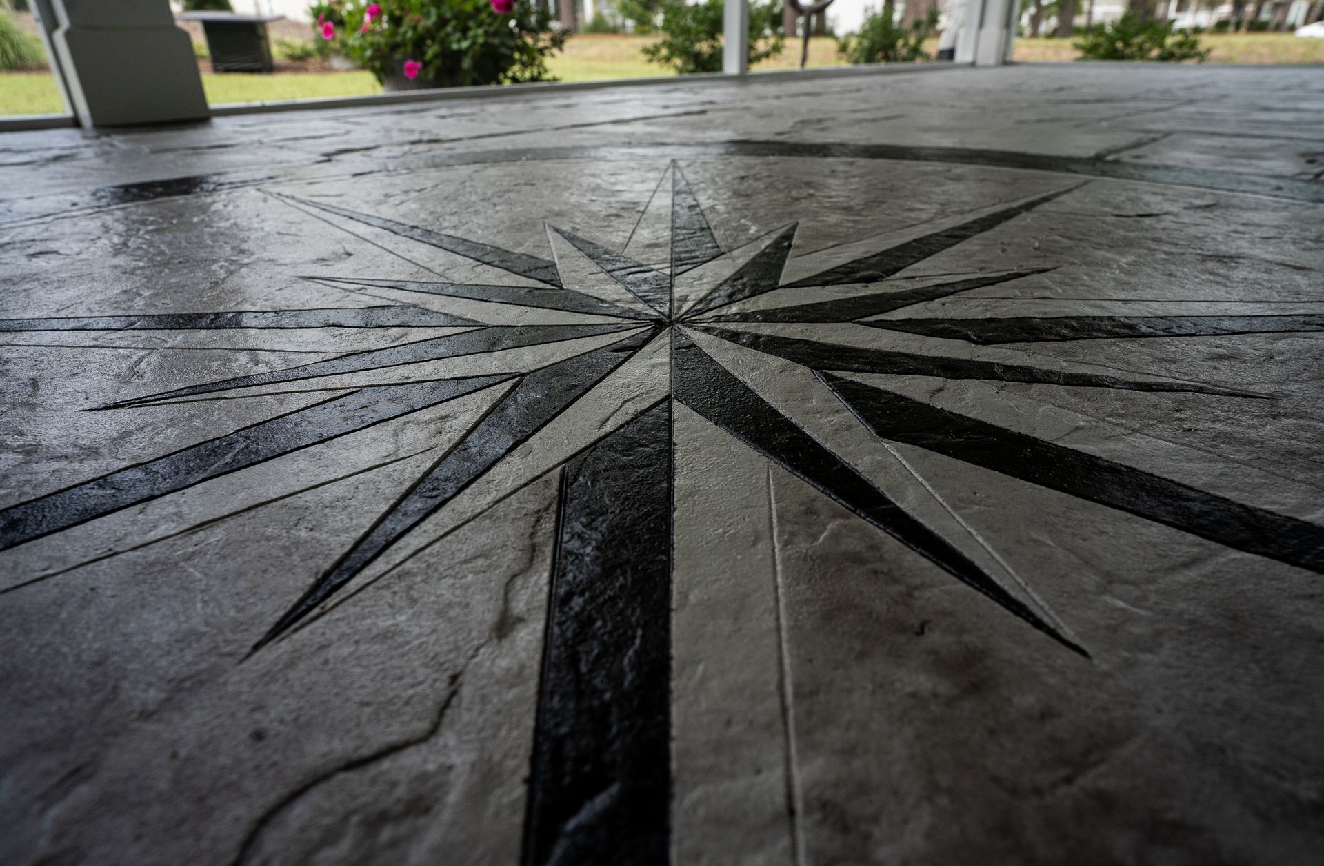 Dark stone floor with a large engraved compass rose design, seen from a low angle outdoors