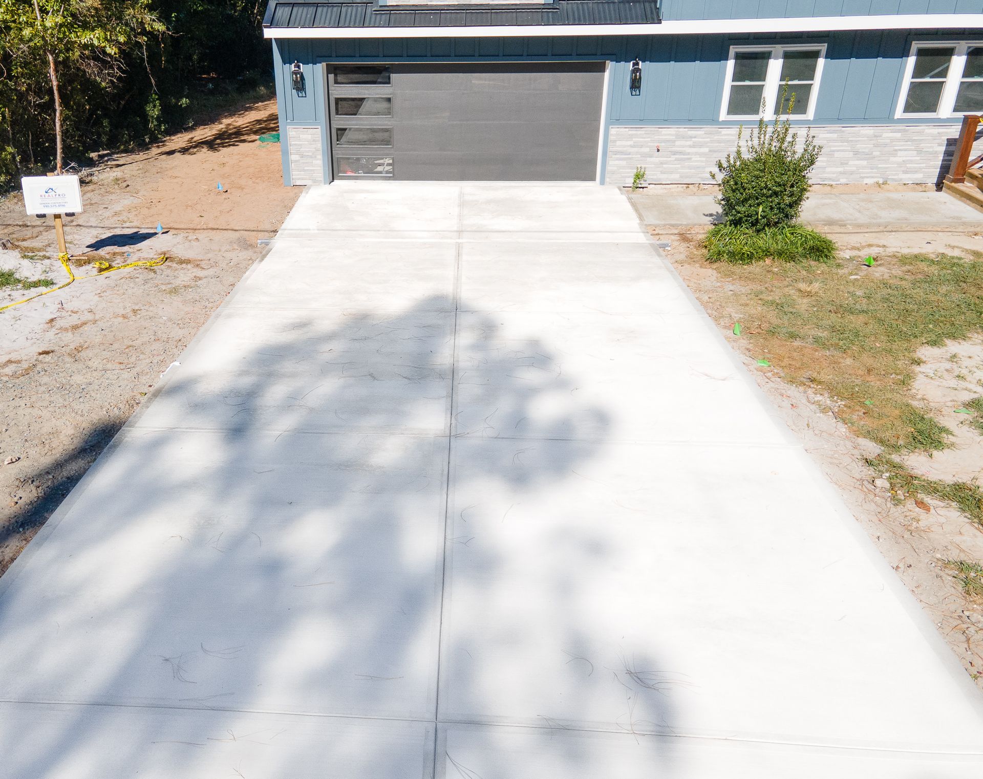 Concrete driveway leading to a blue house with a gray garage door and small front yard