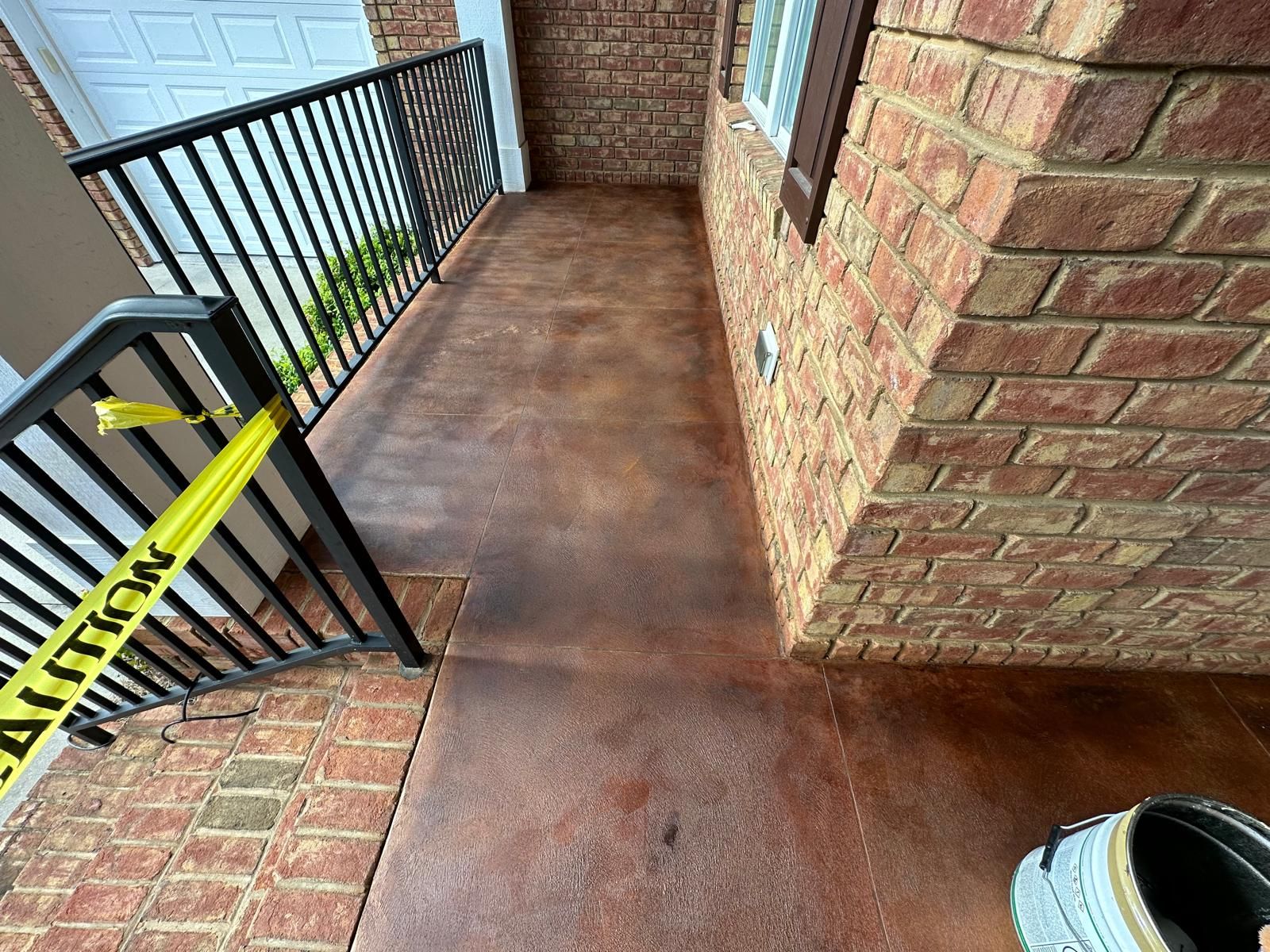 Brick porch with black railing, yellow caution tape, and a wet brown floor near a doorway.