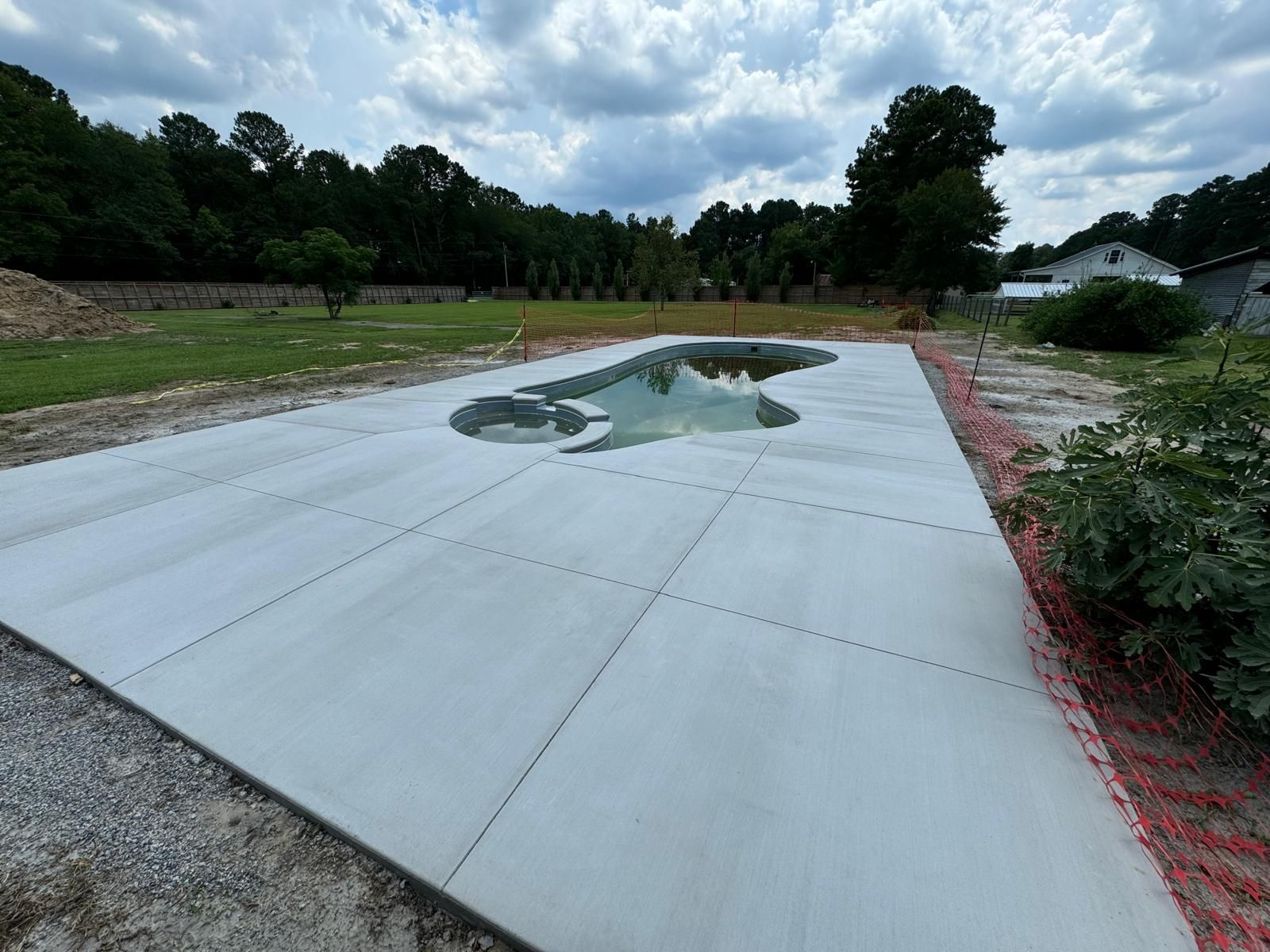 Concrete slab with a puddle in a landscaped outdoor area under cloudy sky