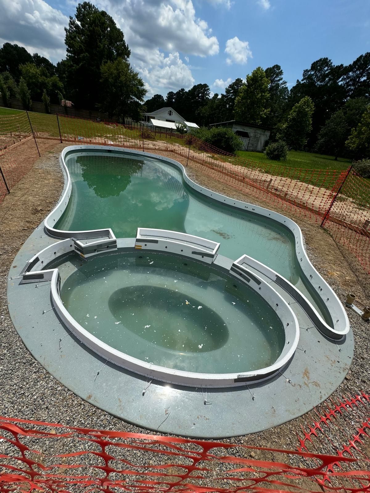 Circular and rectangular in-ground pools under construction behind orange safety fencing