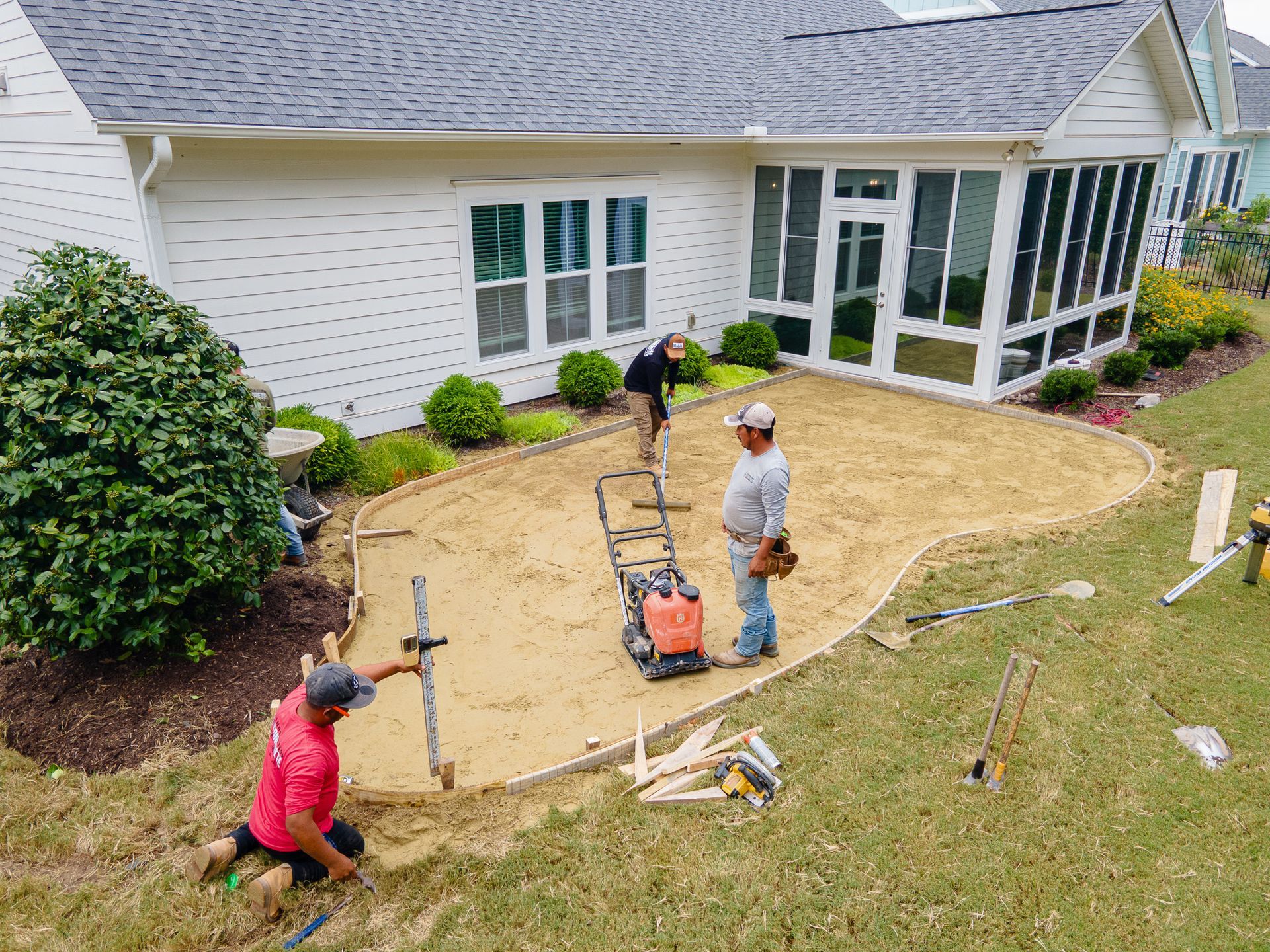 Workers installing a curving lawn edge beside a white house and screened porch