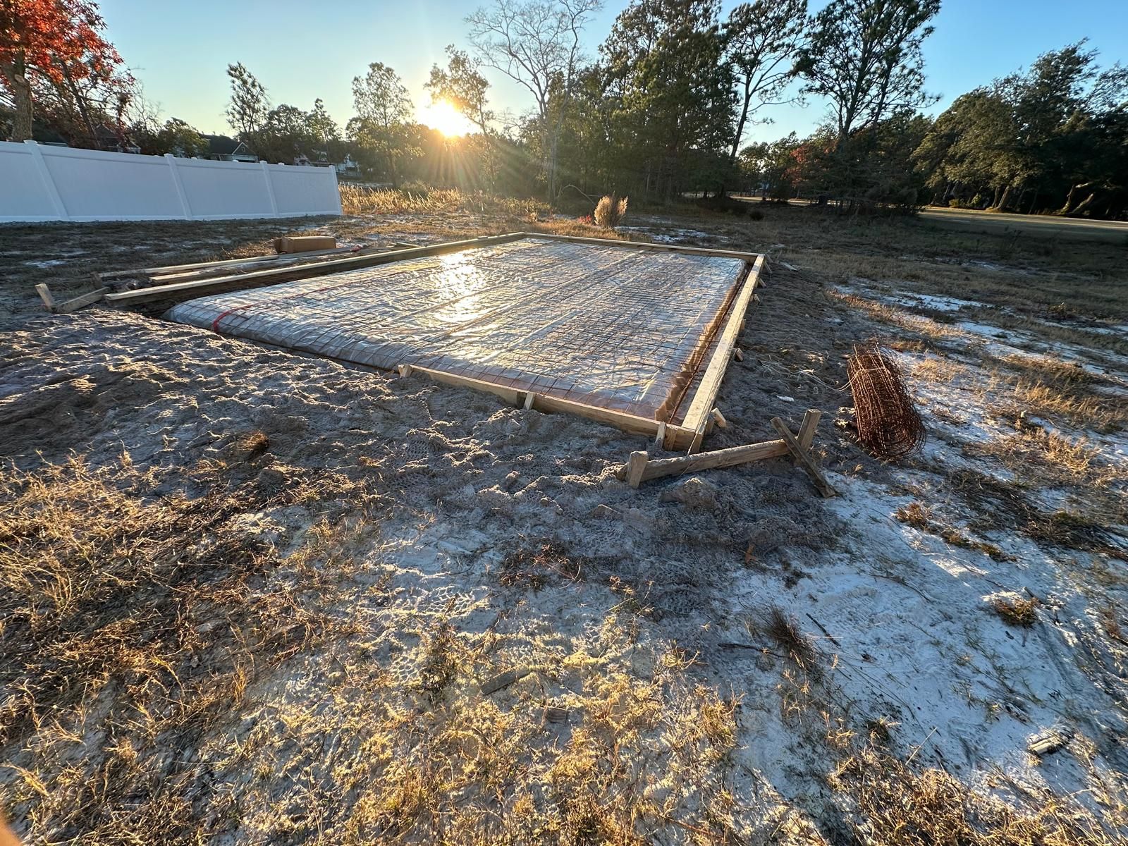 A framed concrete slab foundation in a cleared wooded lot at sunrise.