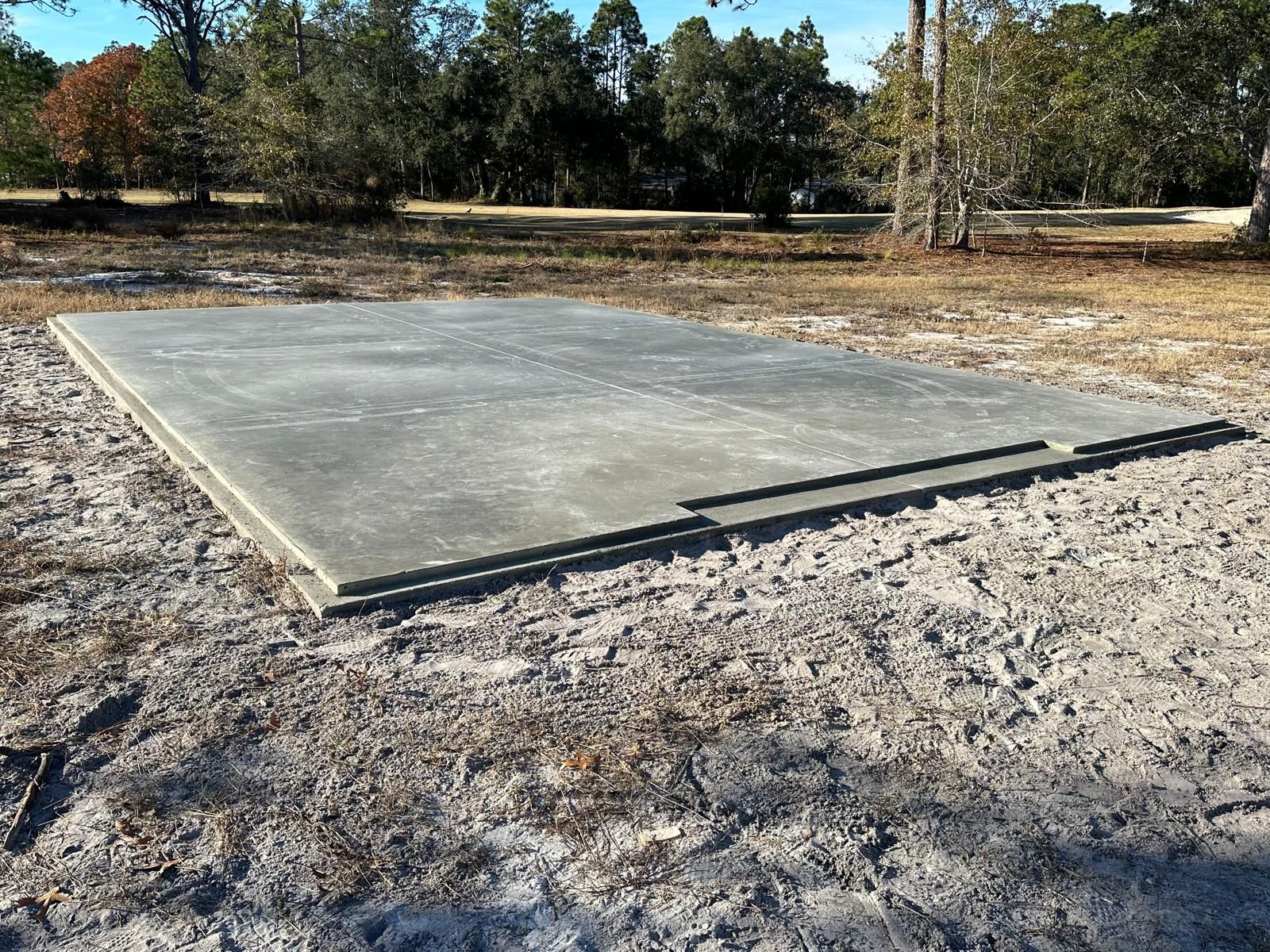 Concrete slab in a wooded clearing, surrounded by gravel and dry grass.