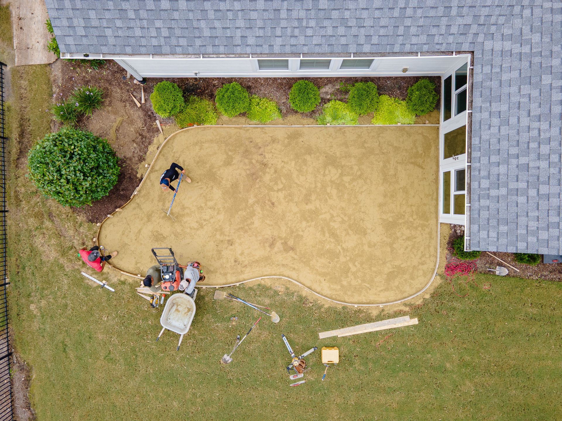 Overhead view of a sandy yard beside a house, with several workers and tools near the edge.