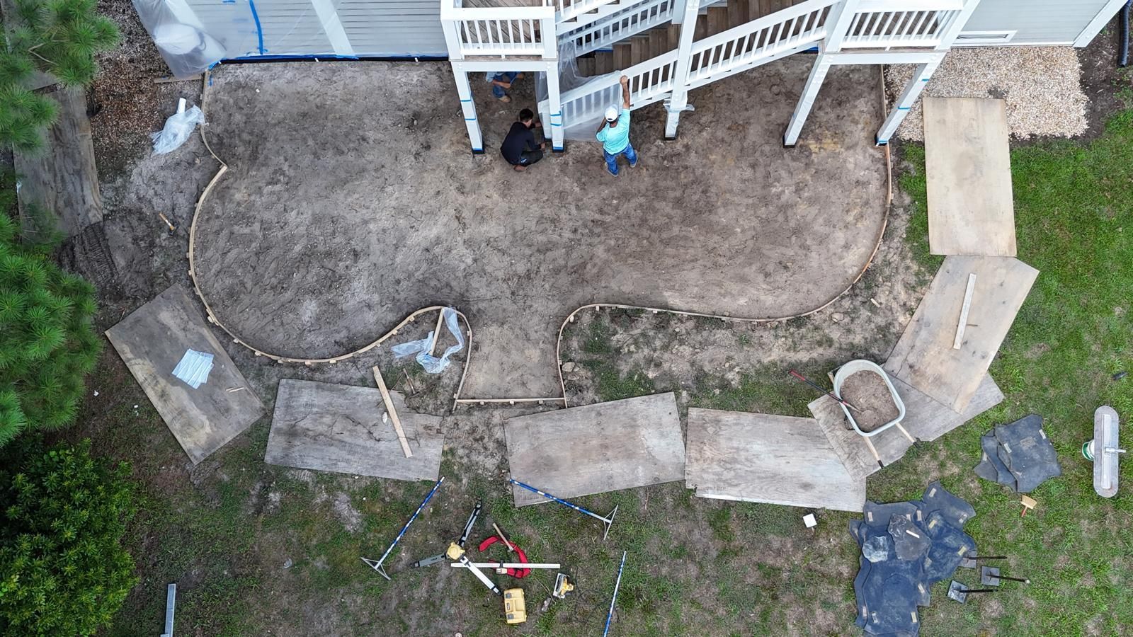 Aerial view of a backyard with a dirt garden bed, stepping stones, and a white fence and porch.