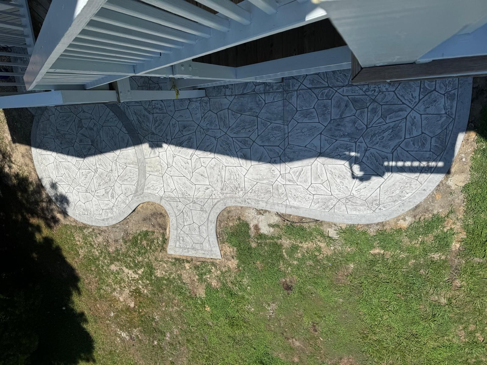 Overhead view of a house edge with a curved stone patio and green lawn below