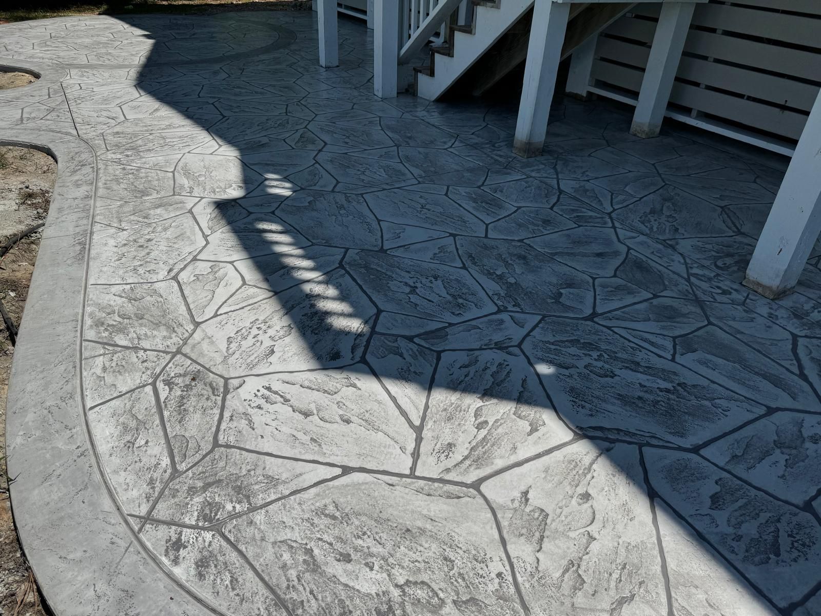 Stamped concrete patio with a curved edge and staircase shadows in bright sunlight