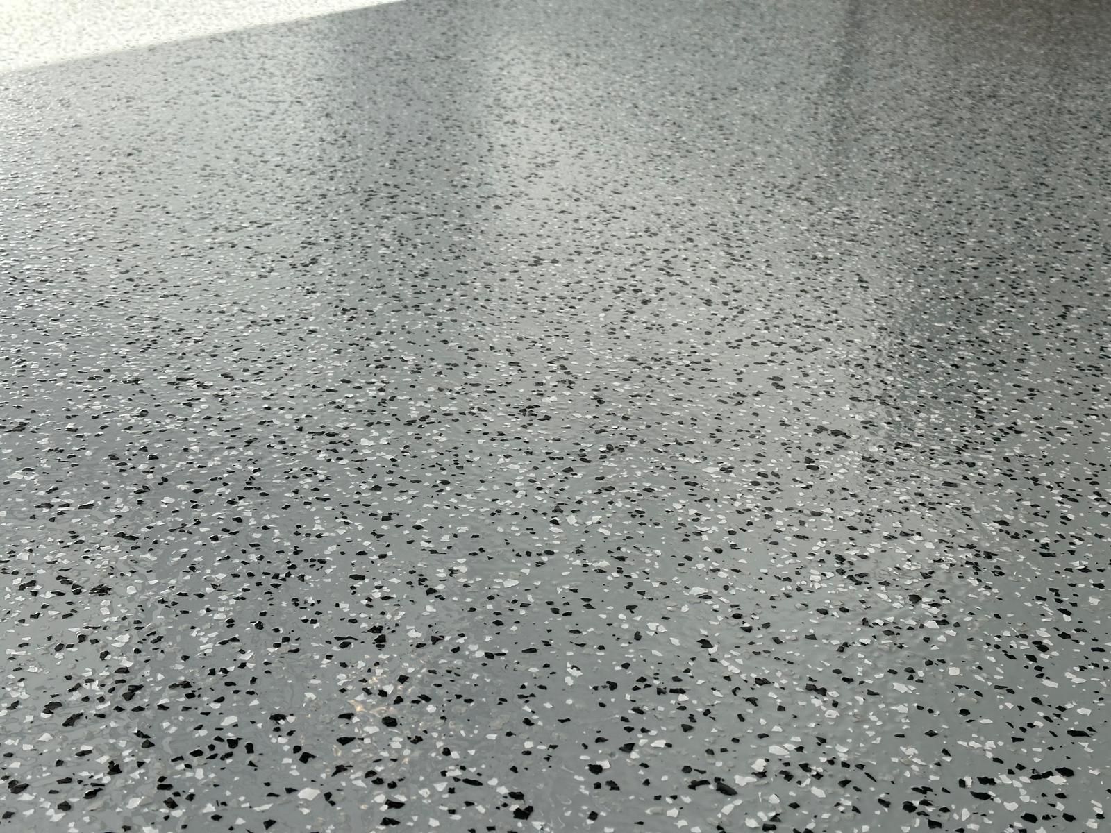 Close-up of a wet gray speckled pavement surface with rain droplets.
