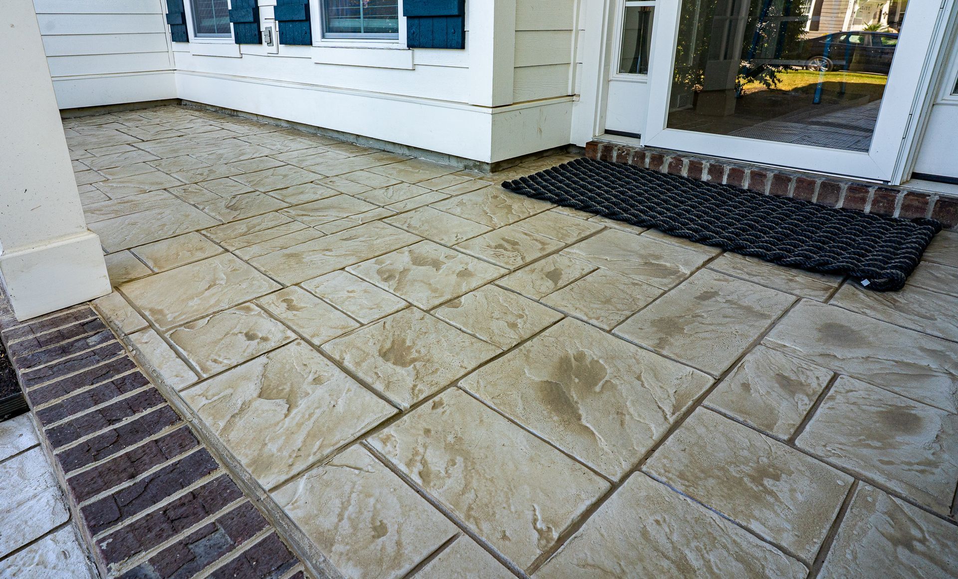 Stone patio beside a white house with brick edging and a front door