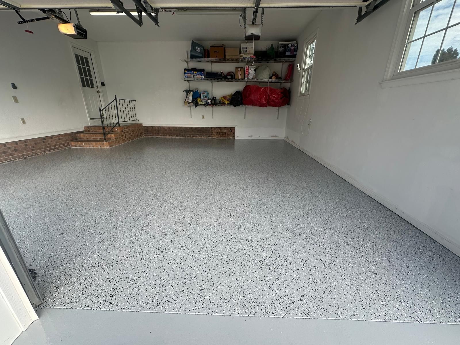 Empty garage with speckled epoxy floor, white walls, shelves, and a window on the right.