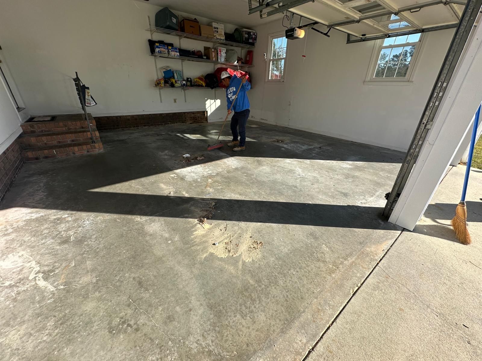 Person standing in a garage with shelving, a ladder, and bright sunlight on the concrete floor