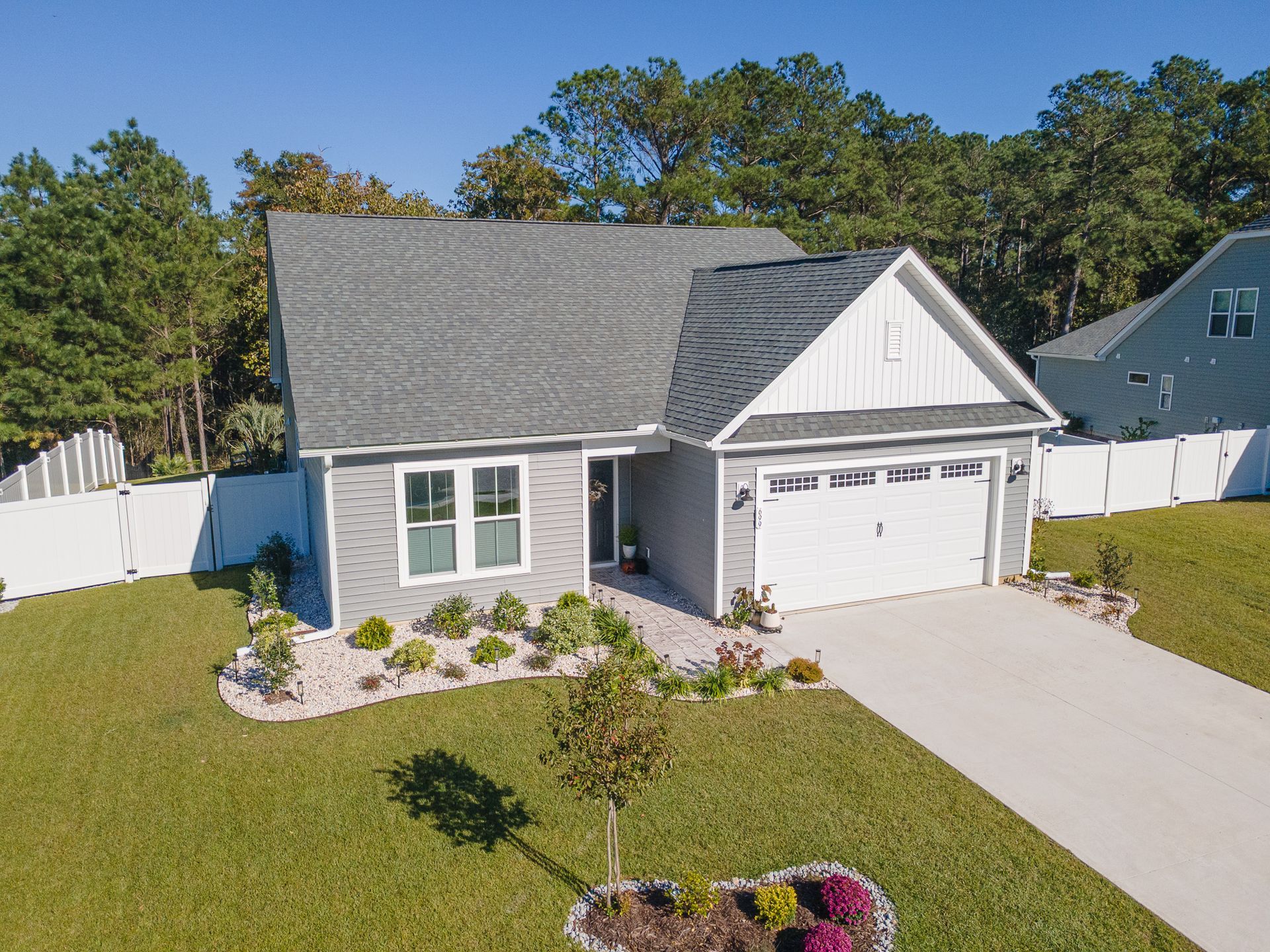 Suburban white house with gray roof, front lawn, and two-car garage on a sunny day