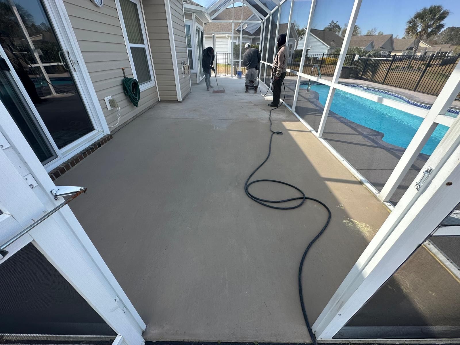 Covered backyard patio with a coiled hose, white railings, and a swimming pool alongside the house.