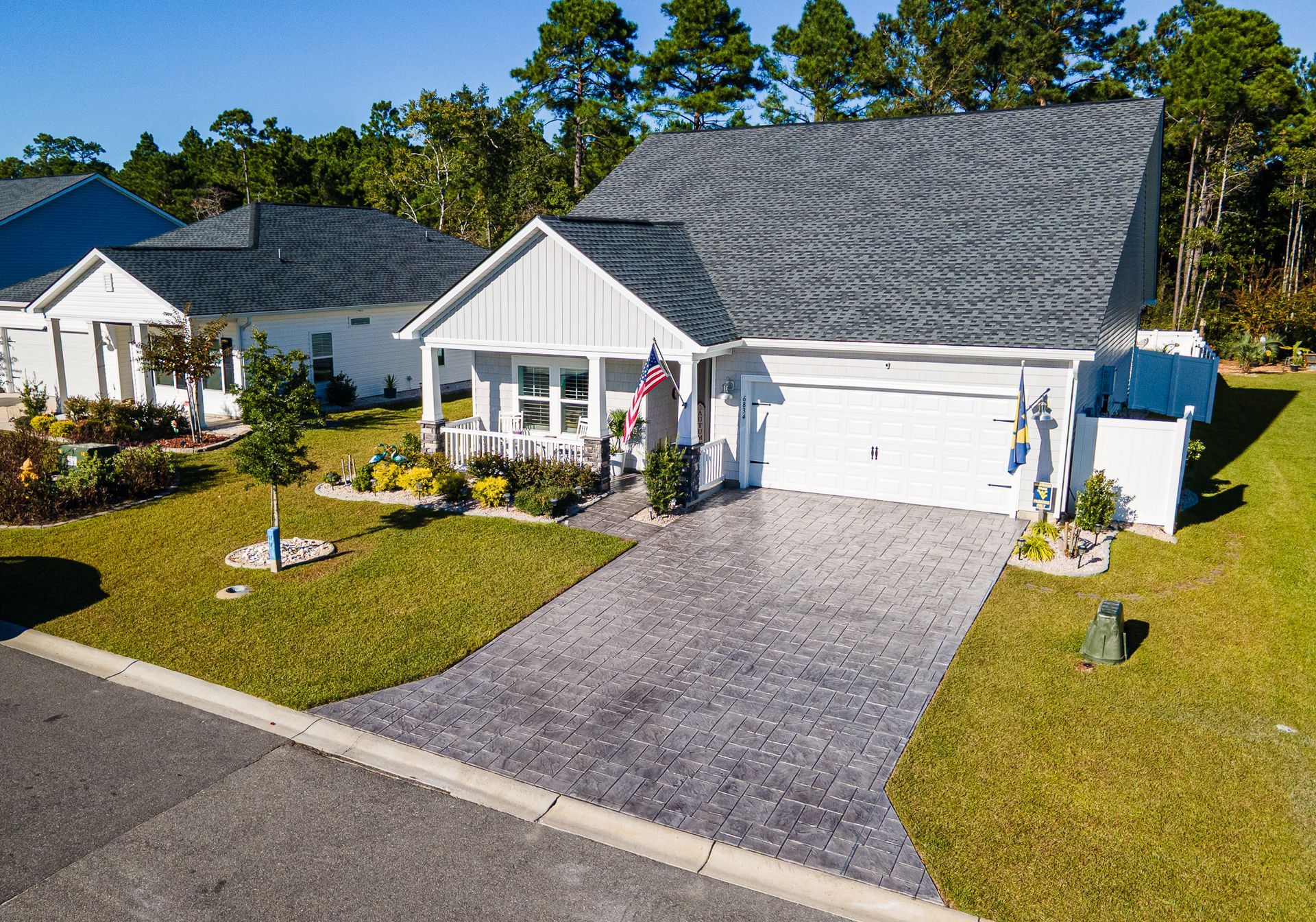 Suburban white house with gray roof, double garage, and a long brick driveway on a sunny day