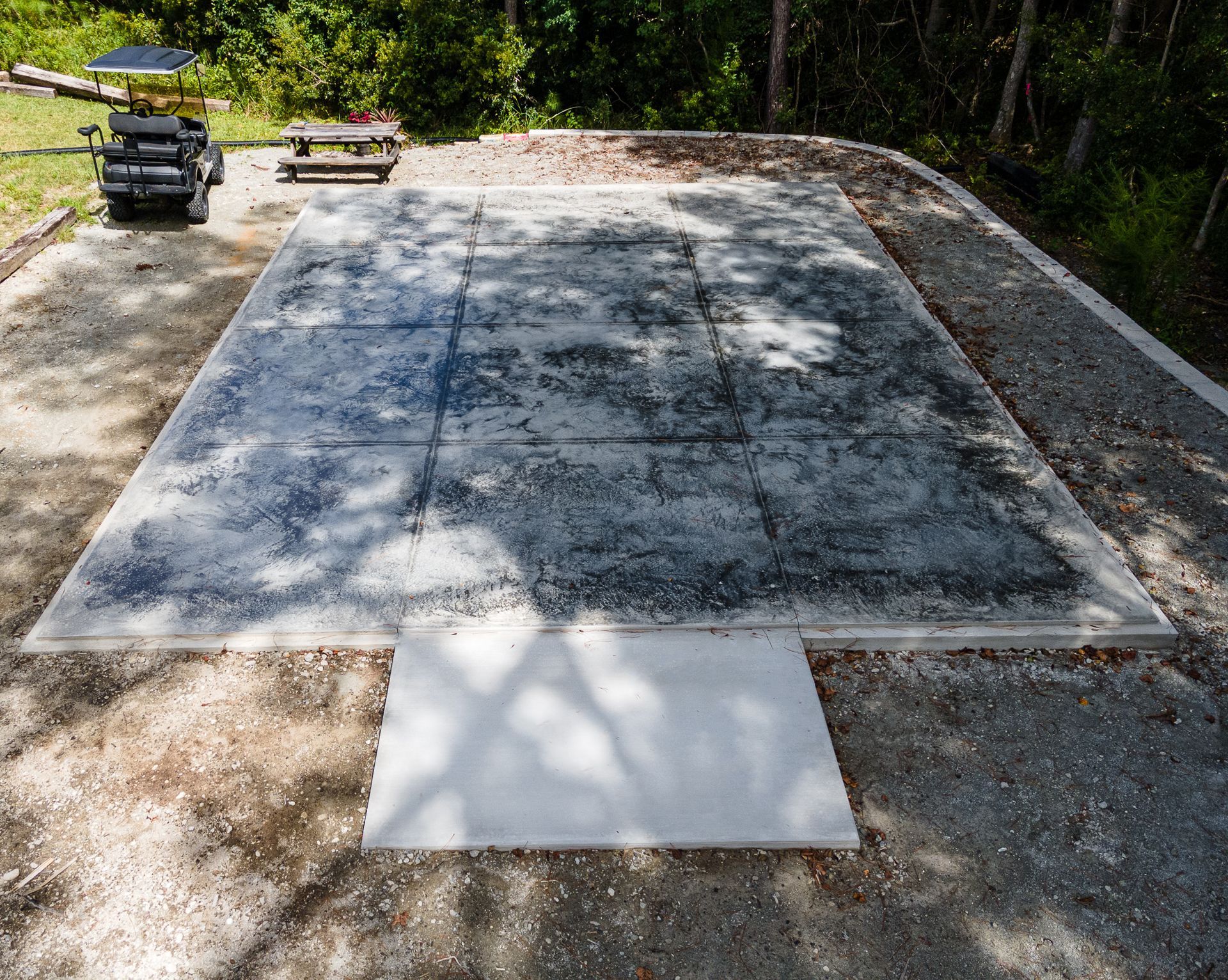 Concrete slab foundation in a wooded area with a pickup truck and wheelbarrow nearby