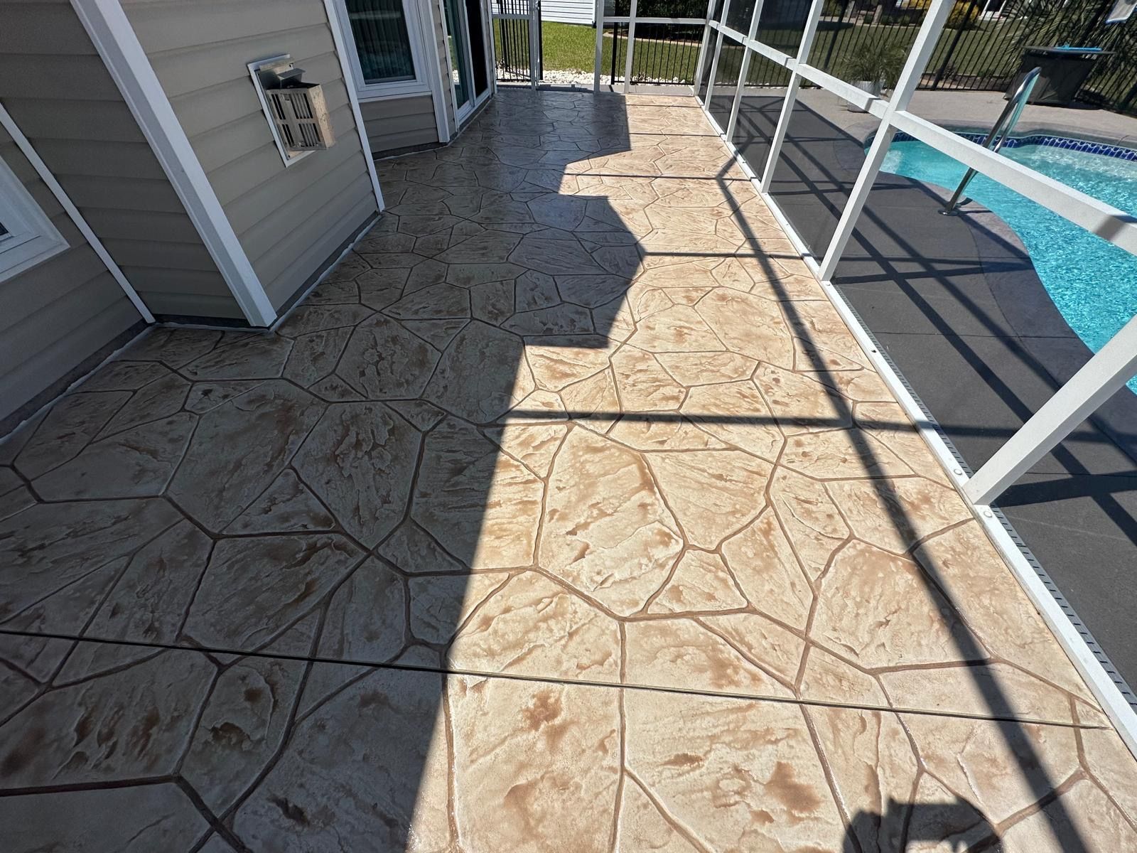 Sunlit stamped-concrete patio beside a pool and house exterior, with white railing and shadows.