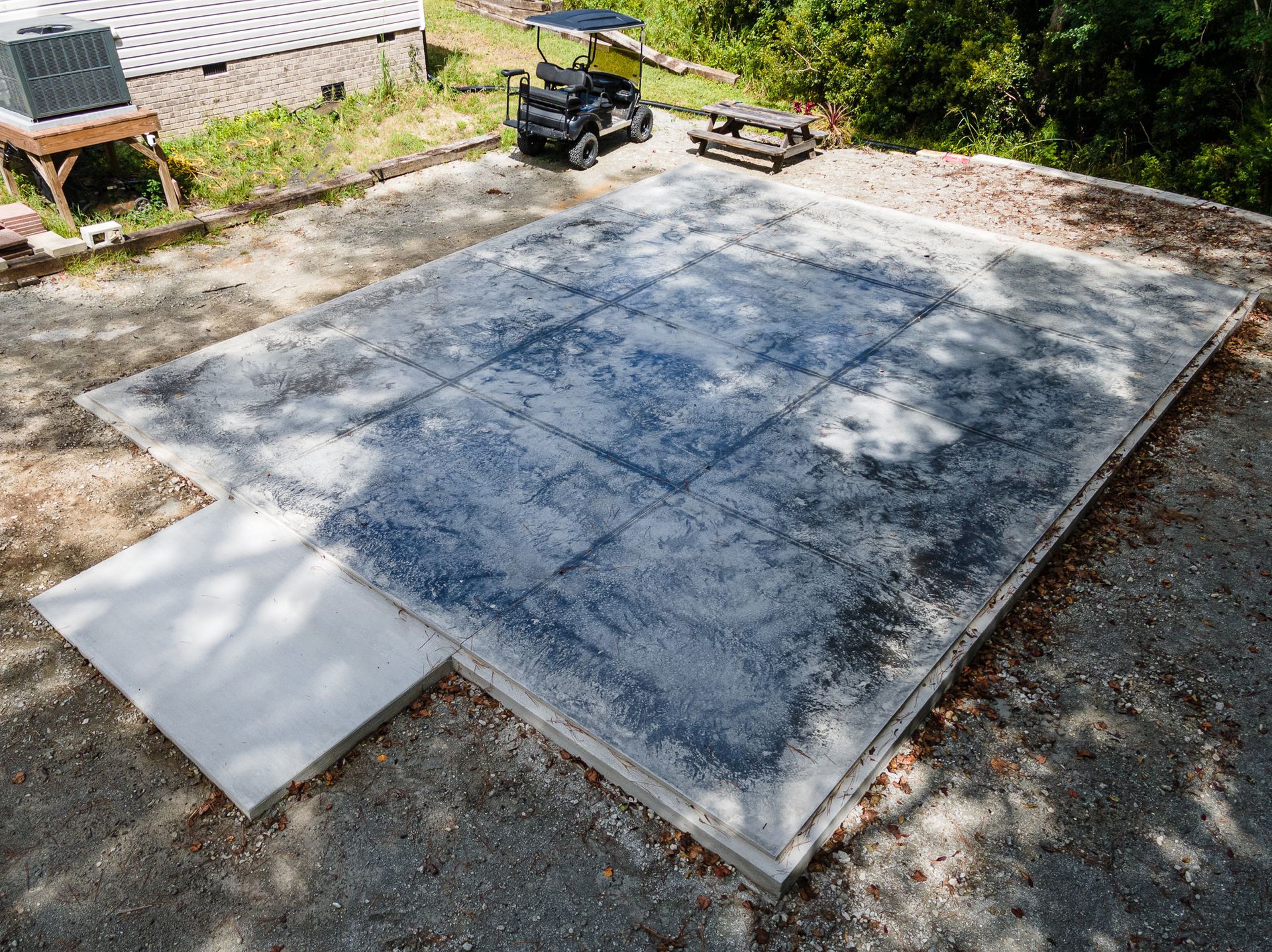 Freshly poured concrete slab in a gravel yard with a small machine and tools nearby