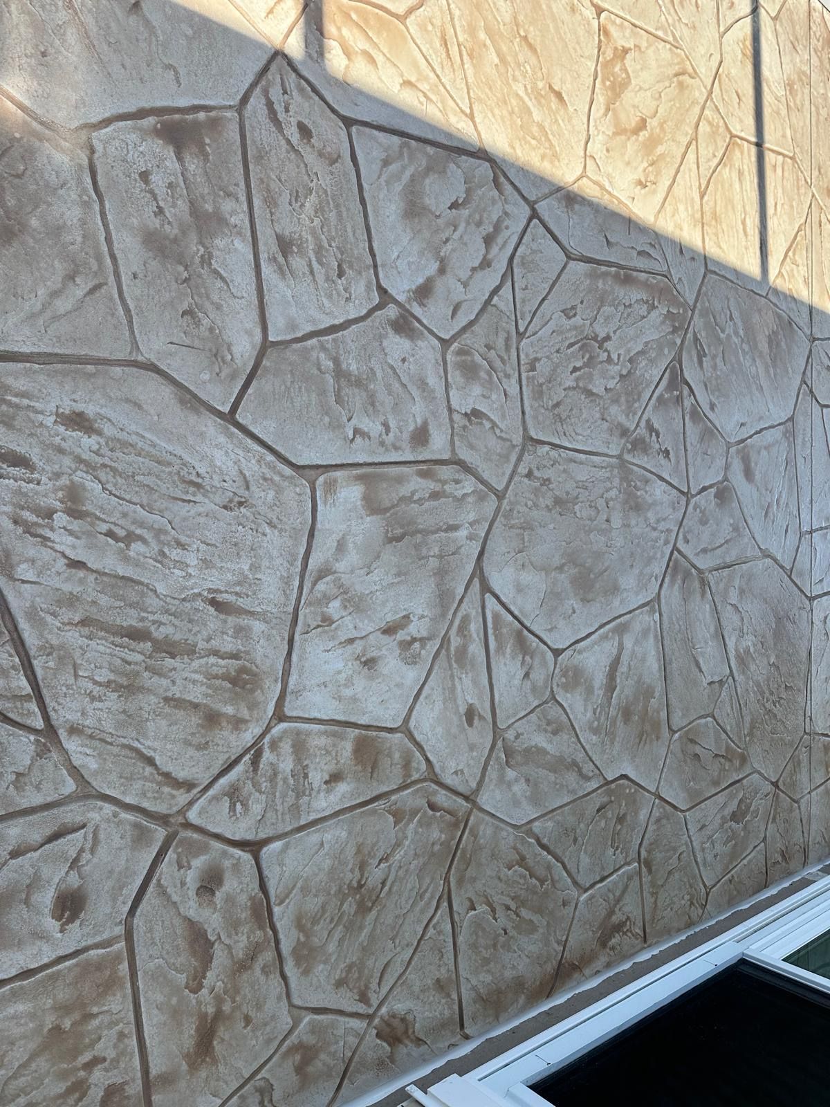 Stone-textured beige wall with diagonal sunlight and a white window frame at the bottom edge