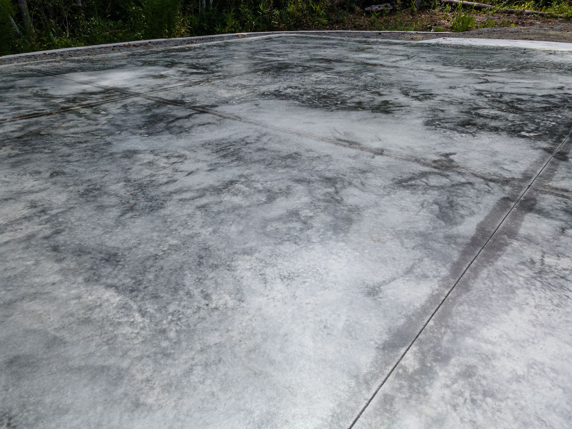 Cracked concrete pavement with faint dark lines and a leafy tree line in the background