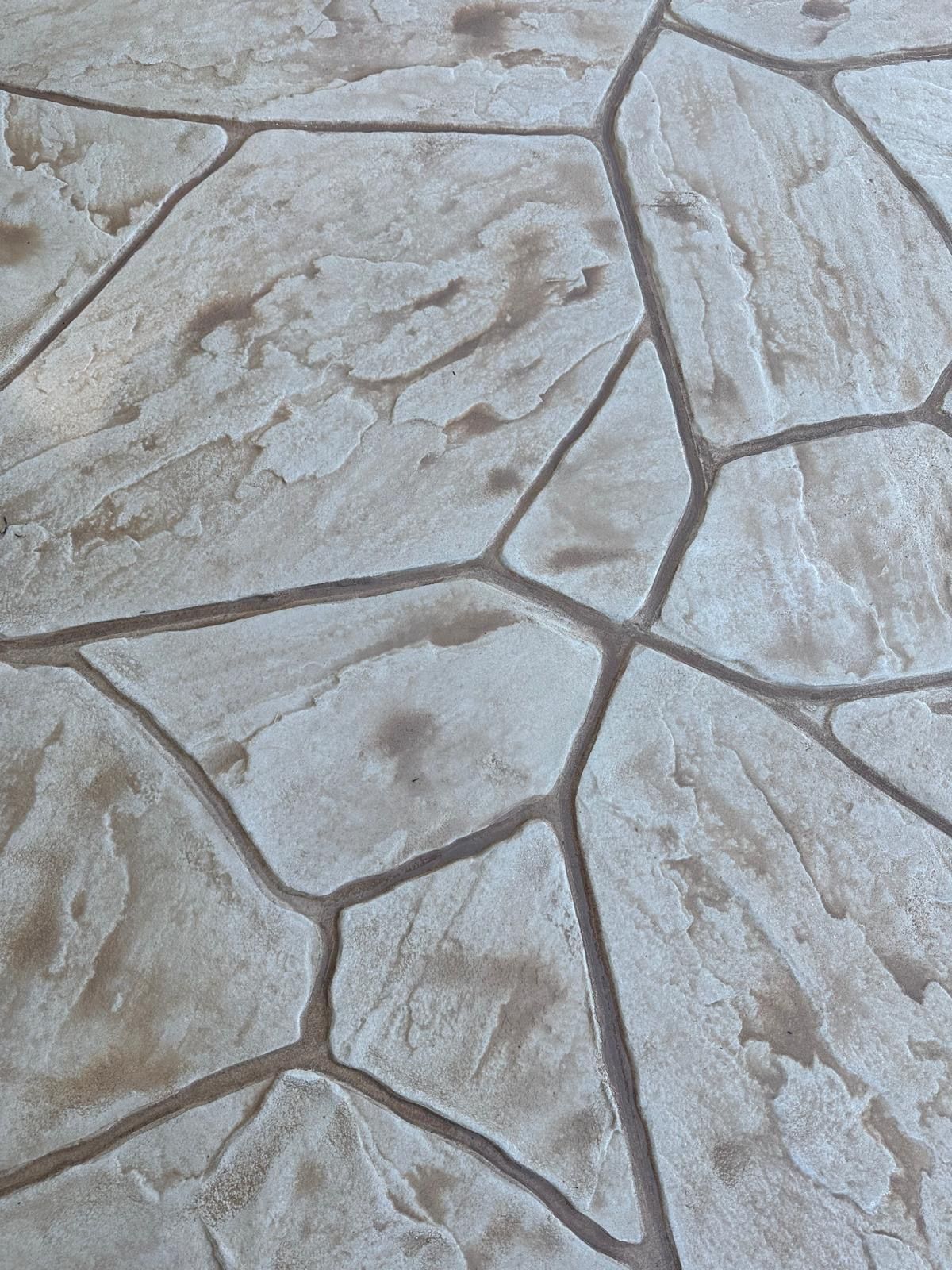 Close-up of light gray stone paving with irregular polygon-shaped tiles and dark grout lines