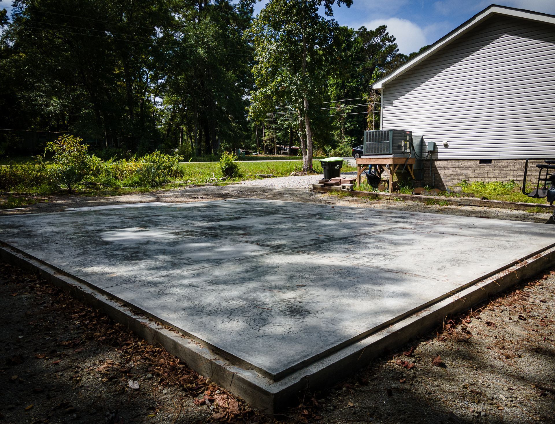 Freshly poured concrete patio beside a white house with outdoor furniture and trees