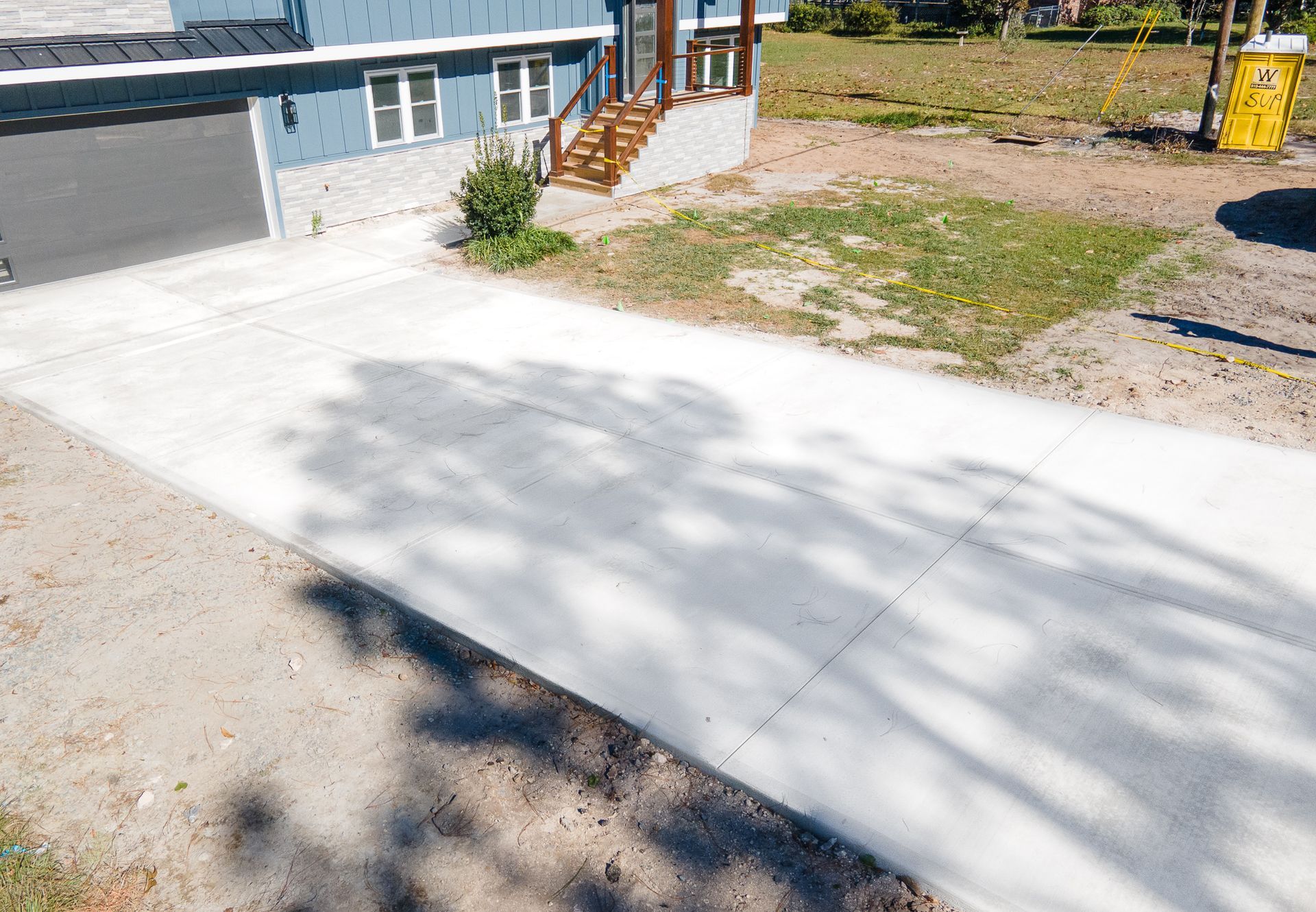 Freshly poured concrete driveway beside a house with a deck and grass yard