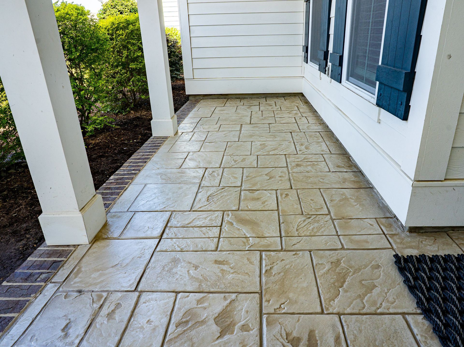 Stone-tiled front porch with white siding, blue shutters, and a black doormat