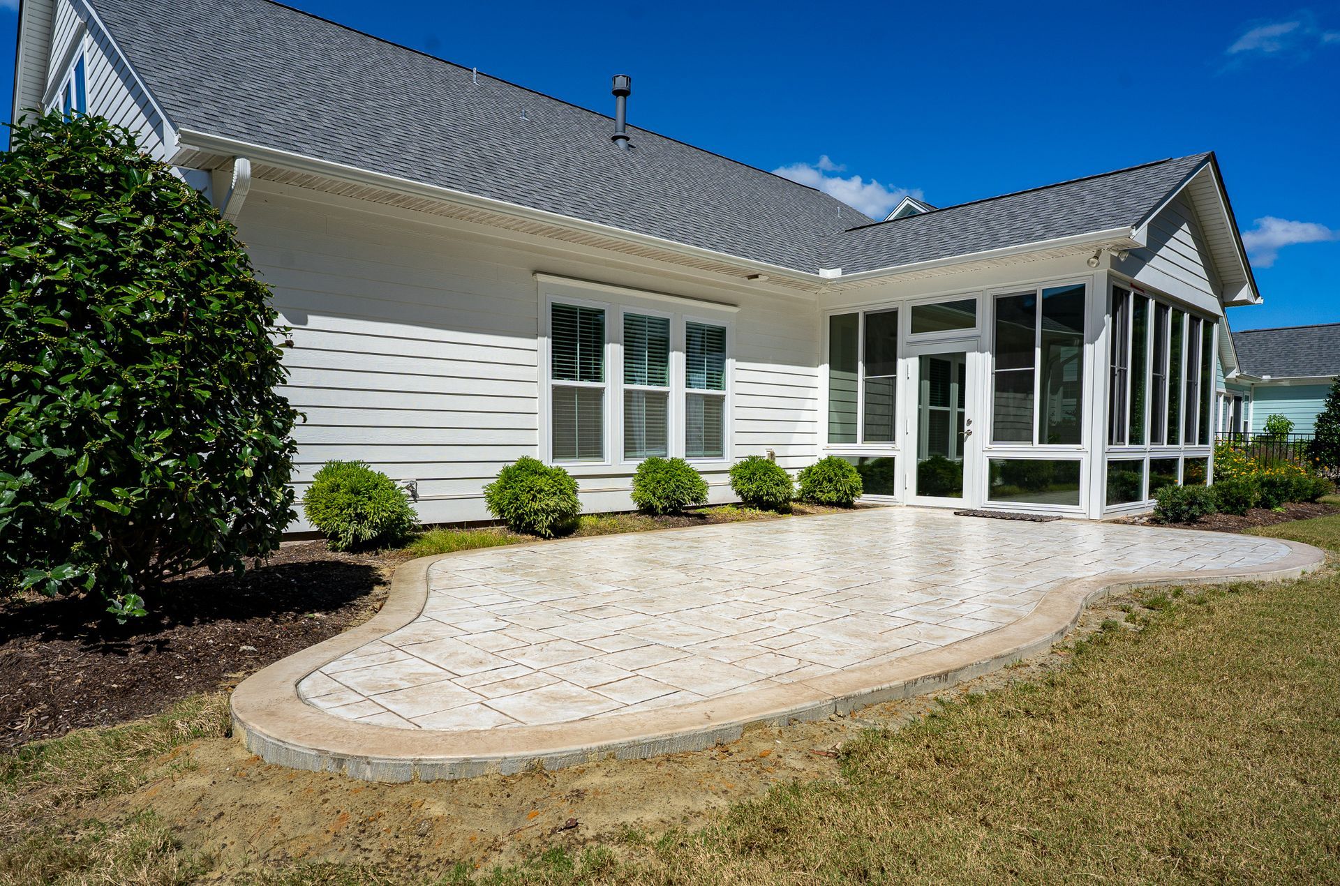 White house with a curved stone patio, screened porch, and green lawn under a clear blue sky