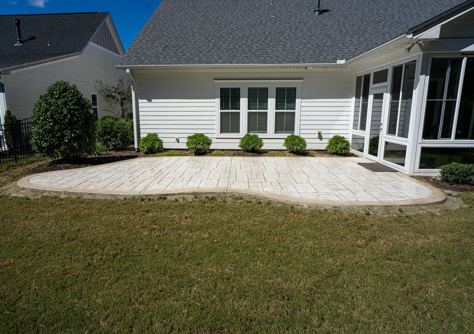 Backyard patio with white pavers, screened porch, and green lawn in front of a house