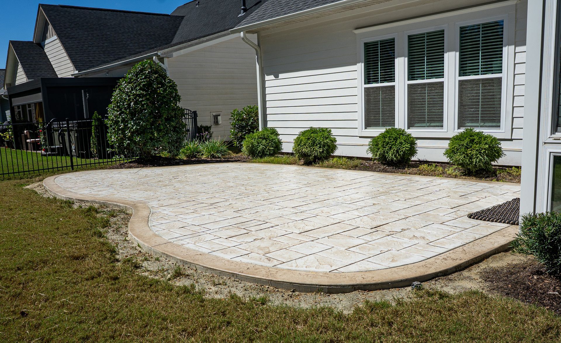 Curved white stone patio beside a suburban house with shrubs and grass