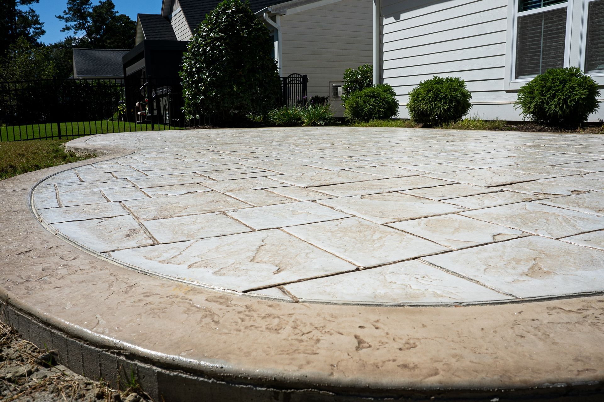 Curved stamped concrete patio beside a house and lawn on a sunny day