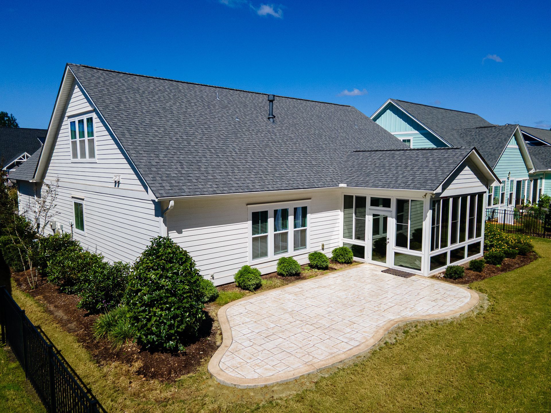 White house with gray shingle roof, screened porch, and curved gravel driveway under a bright blue sky