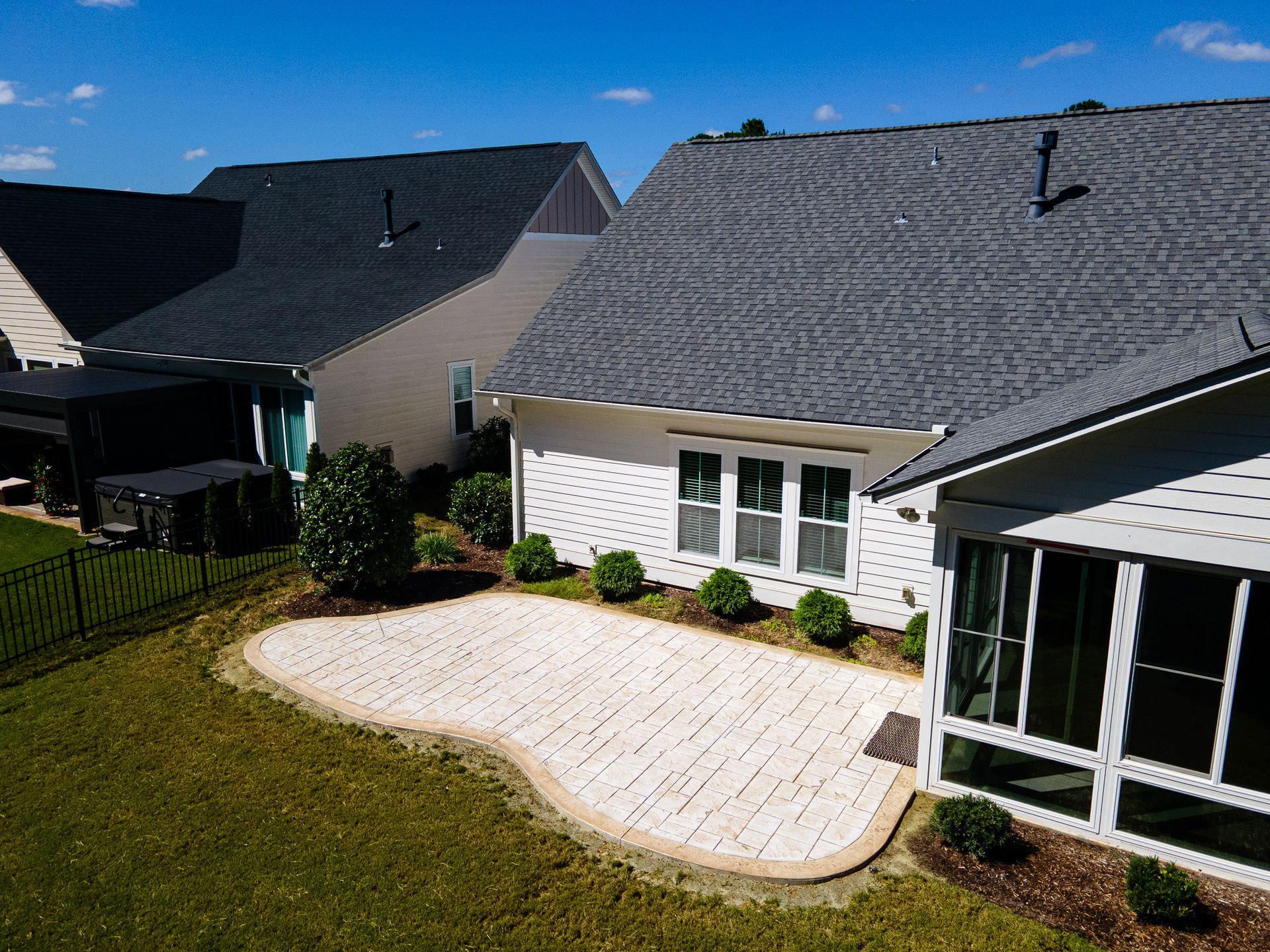Backyard patio with white pavers, green lawn, and a house with gray shingled roof and screened porch