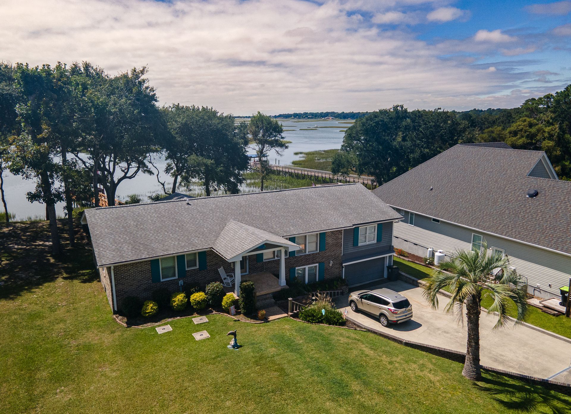 Aerial view of a lakeside house with a gray roof, driveway, lawn, and trees near the water