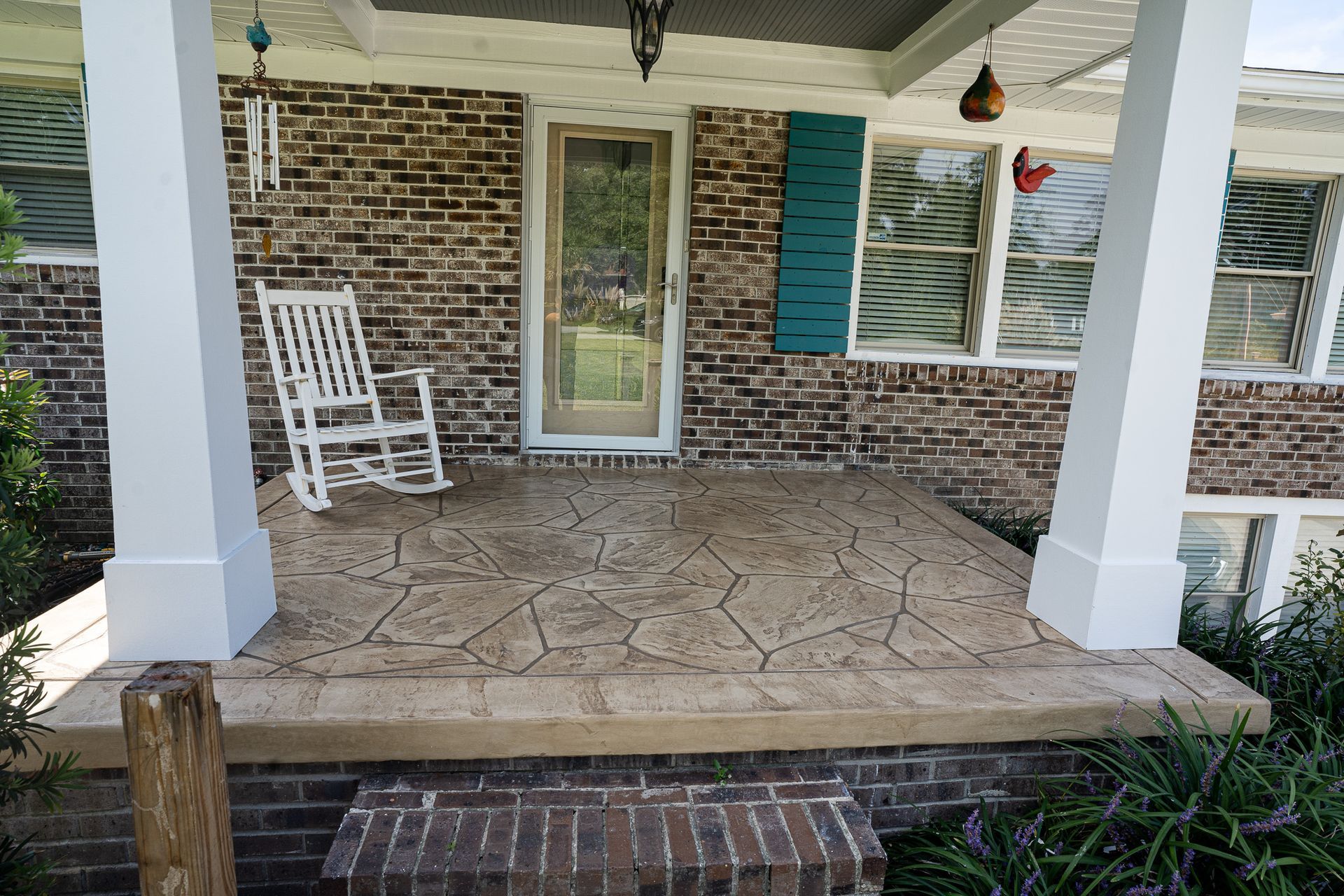 Front porch with brick wall, white rocking chair, and white columns under a covered entry.