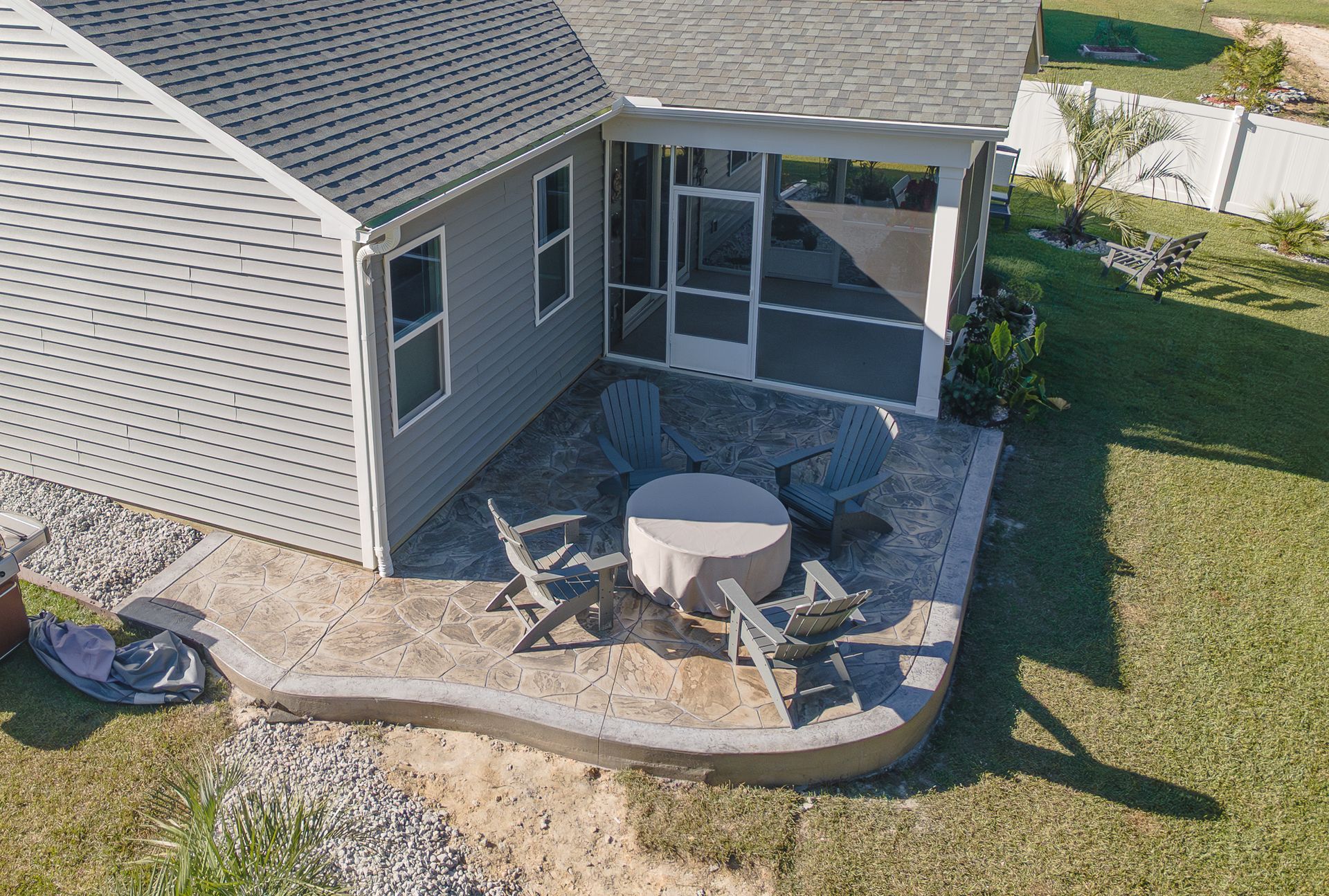 Backyard patio with round table, chairs, screened porch, and a small fire pit beside a house.