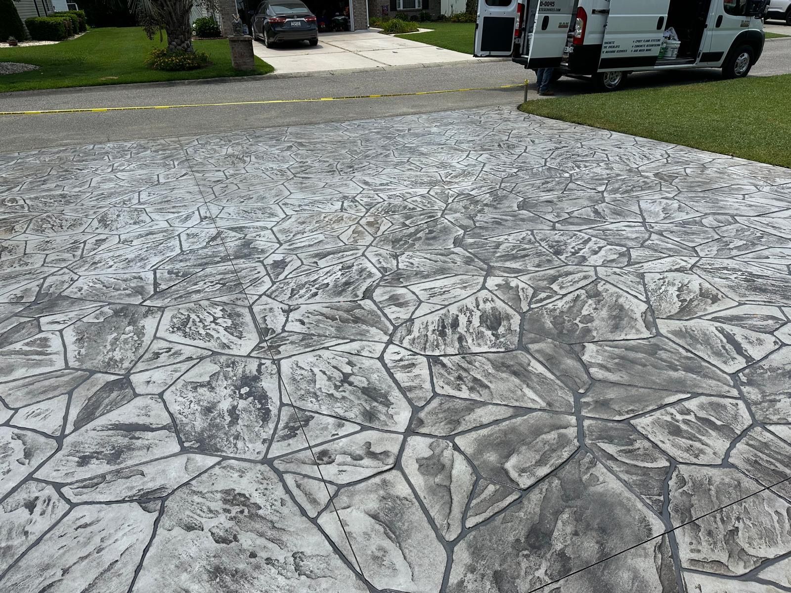 Stamped concrete driveway with irregular stone pattern leading to parked vehicles and a grassy yard