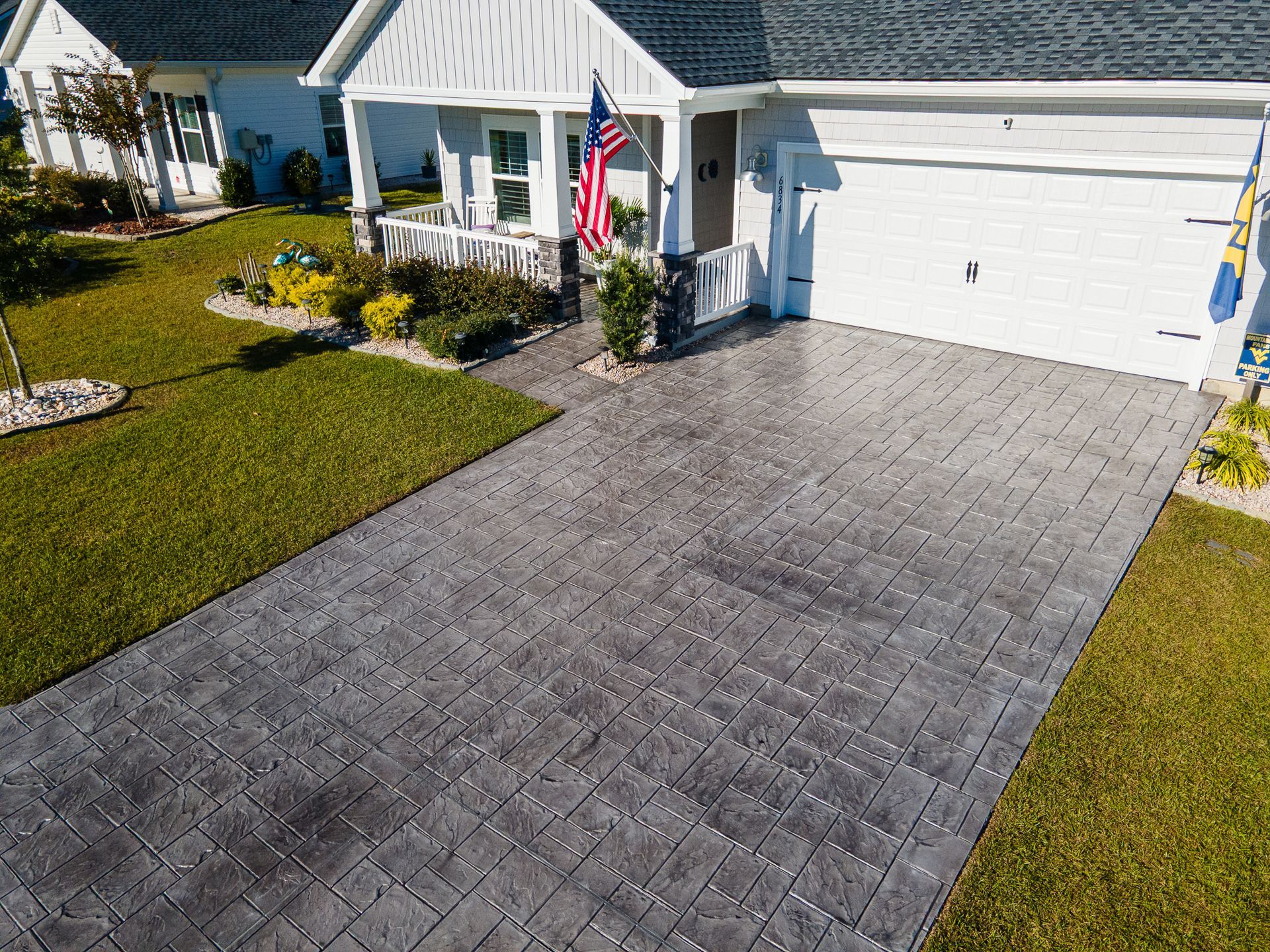 Suburban house with white garage, gray paver driveway, and a U.S. flag by the front door