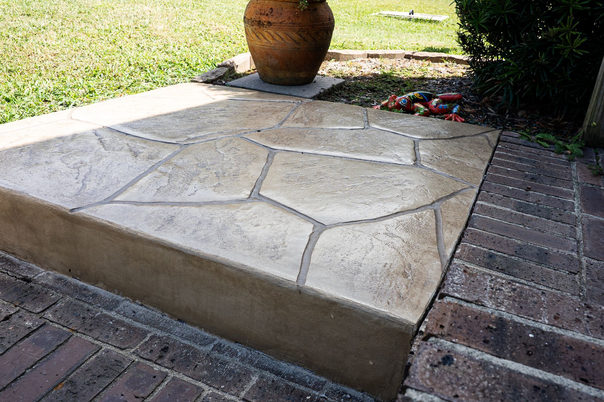 Concrete patio platform with irregular stone pattern, bordered by brick paving and a large terracotta pot.