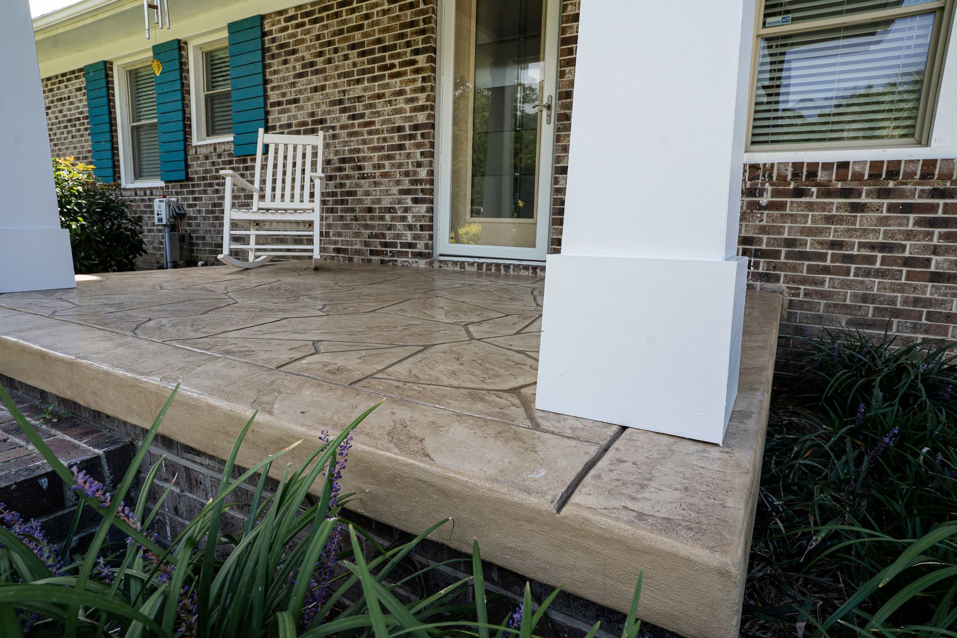 Front porch with stone steps, white columns, brick wall, glass door, and a white rocking chair.