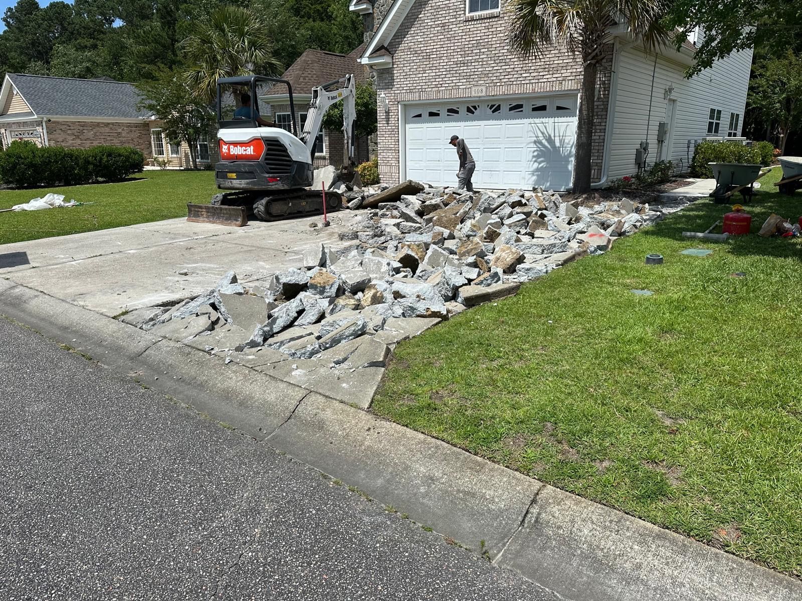House driveway with a small excavator and a pile of broken concrete beside the garage.