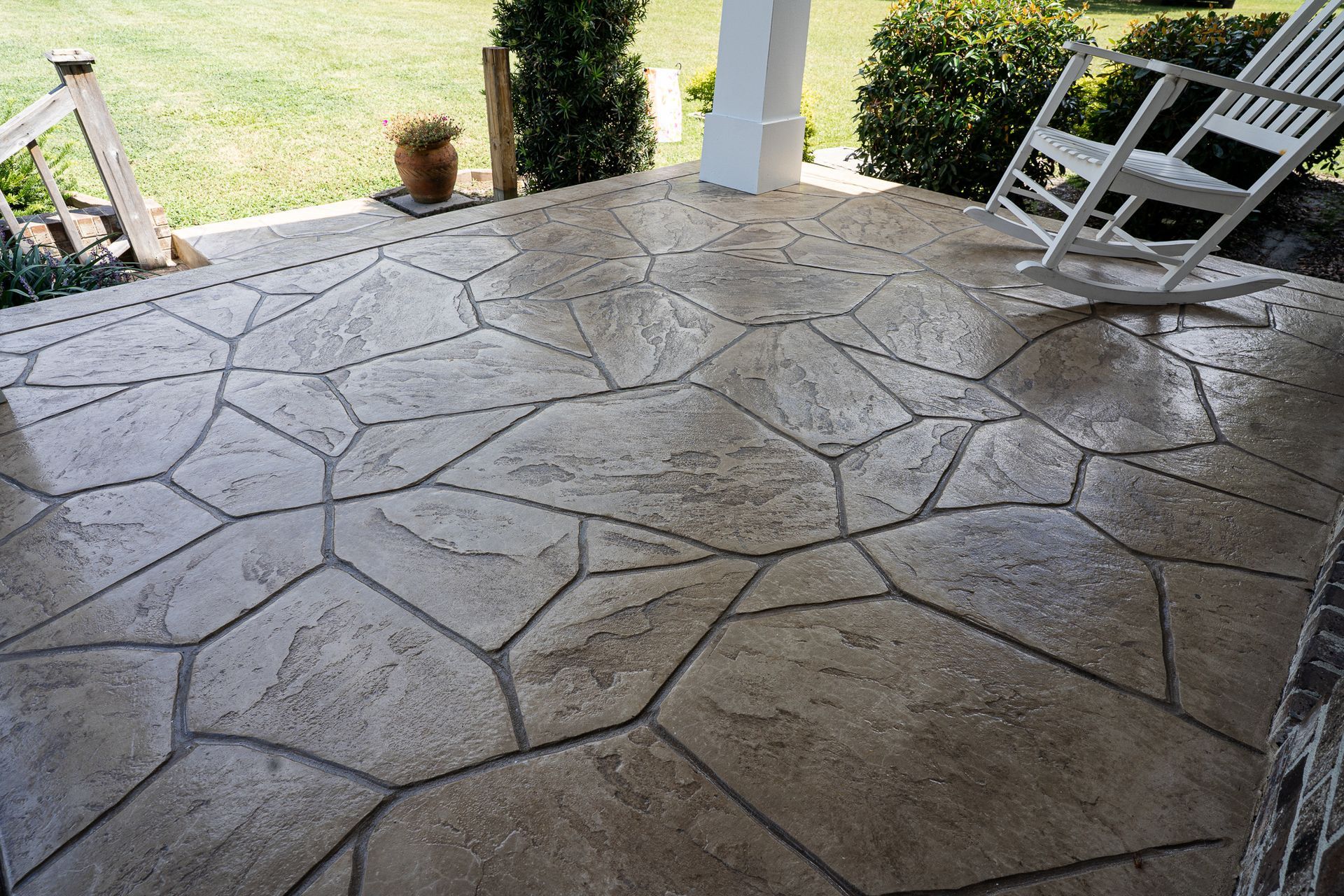 Stamped concrete patio under a covered porch with outdoor chairs and a grassy yard beyond